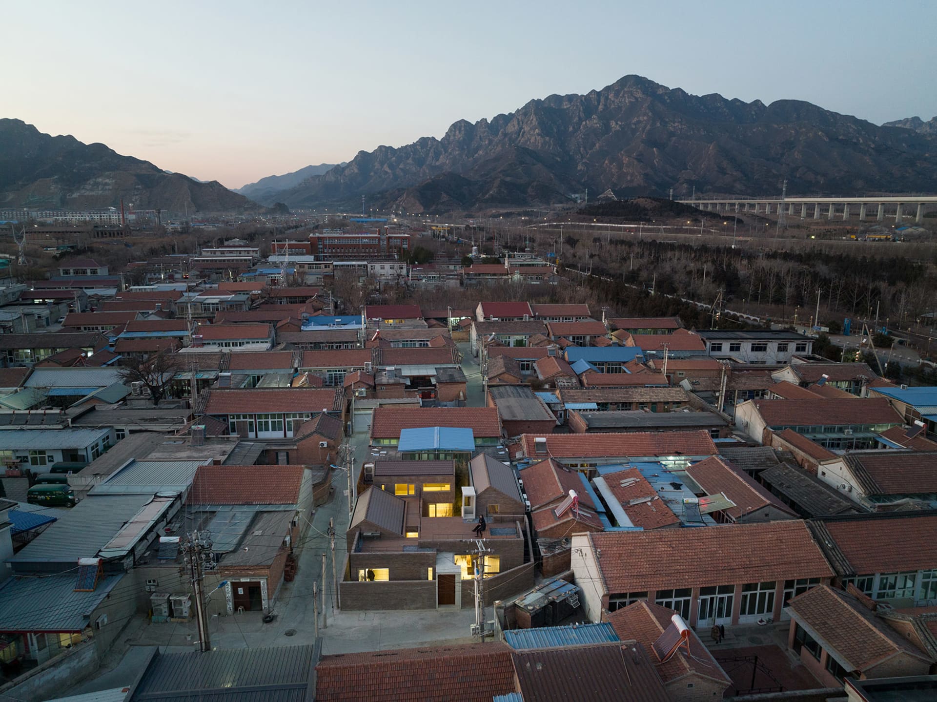 High-angle view of a residential community with ceramic-tiled roofs, surrounded by mountains.