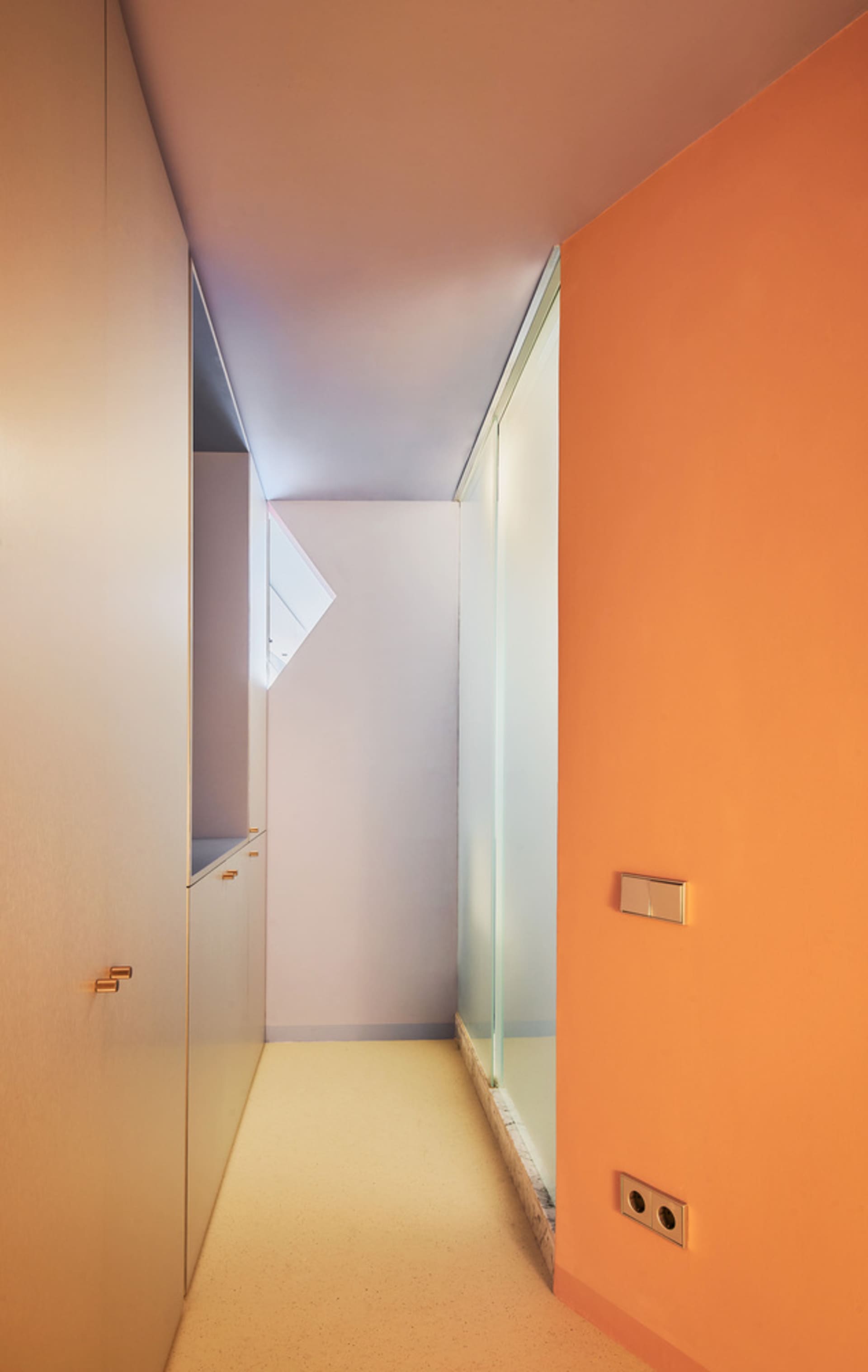 Modern corridor with orange and white walls, glass door, and wooden cabinets.