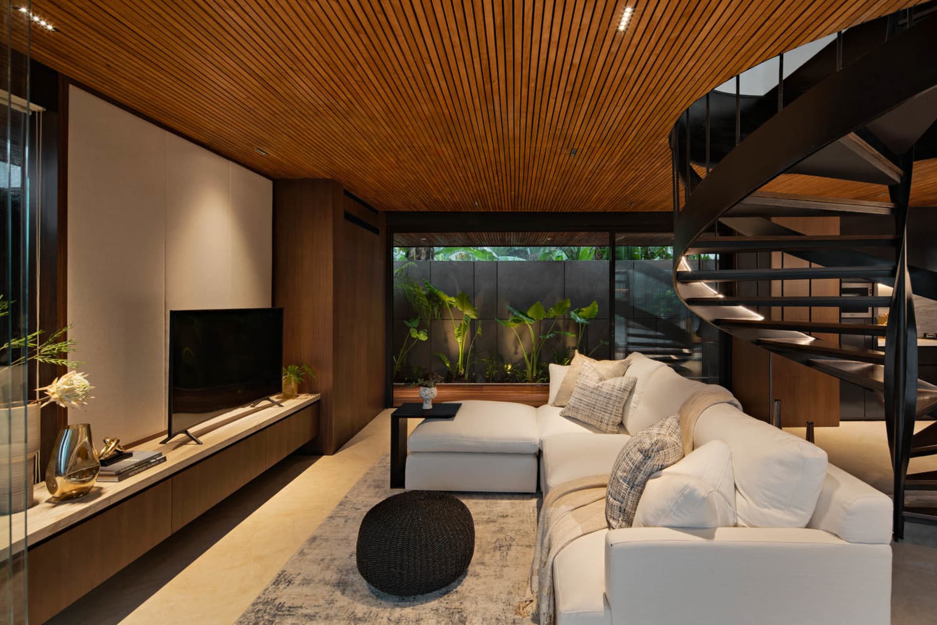 Modern living room with white sectional sofa, wooden ceiling, and spiral staircase.
