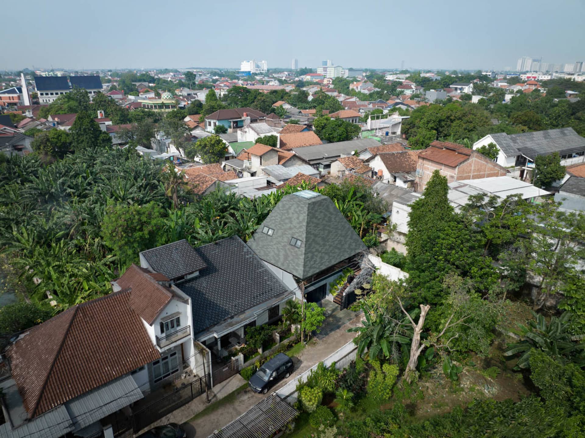 Aerial view of a residential area with concrete, brick, and wooden buildings surrounded by greenery.