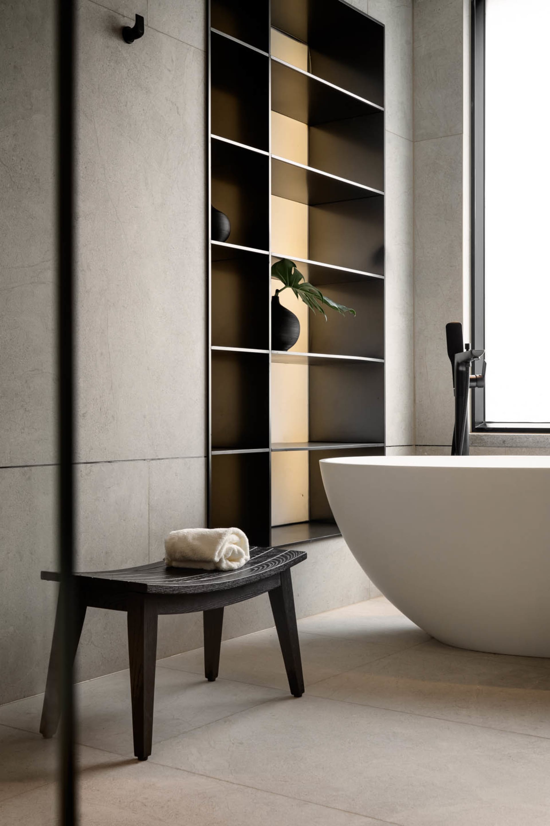 Modern bathroom interior with a concrete tile floor and wall, featuring a white freestanding bathtub and minimalist design el