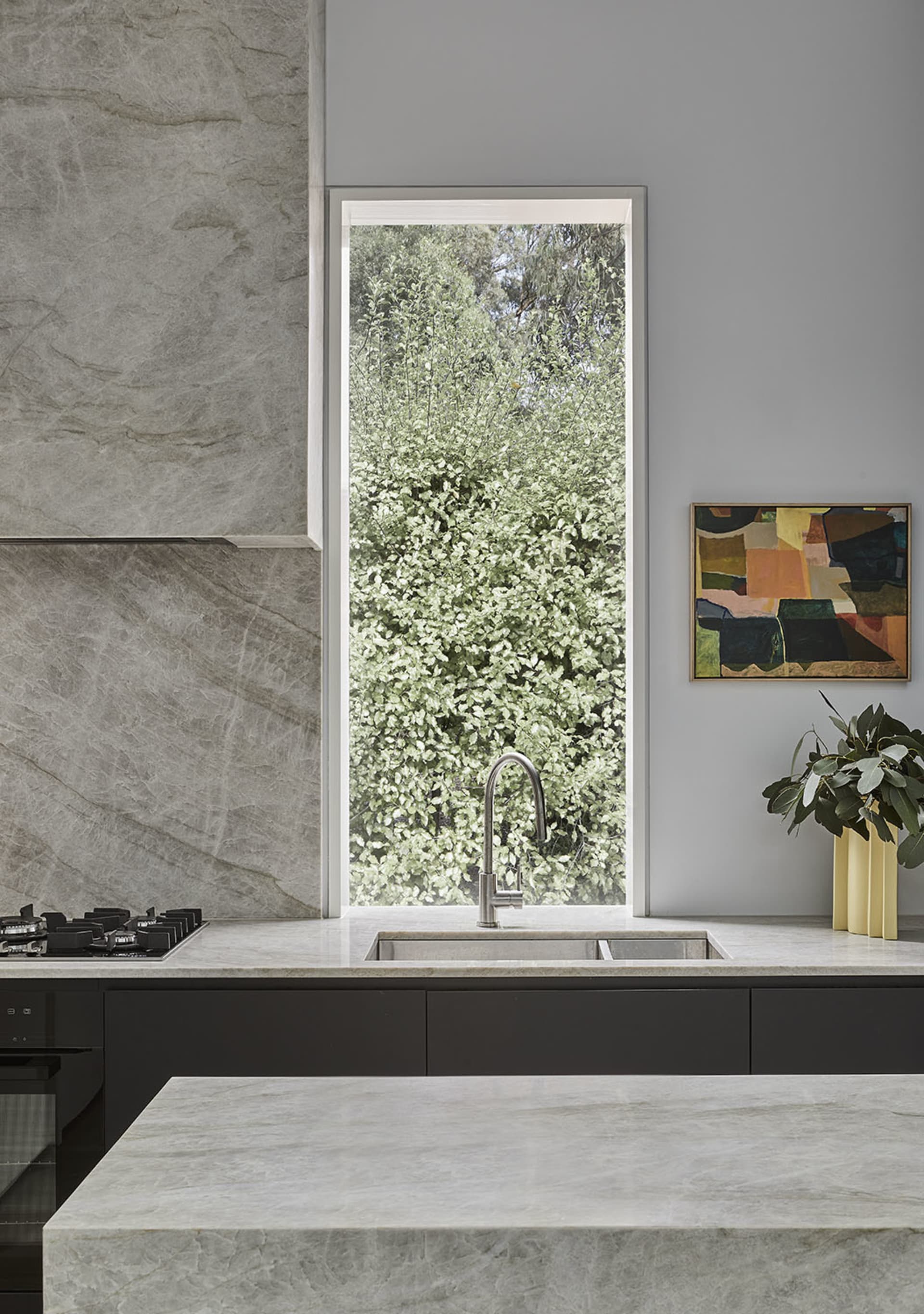 A modern kitchen with marble countertops and a large window overlooking greenery.