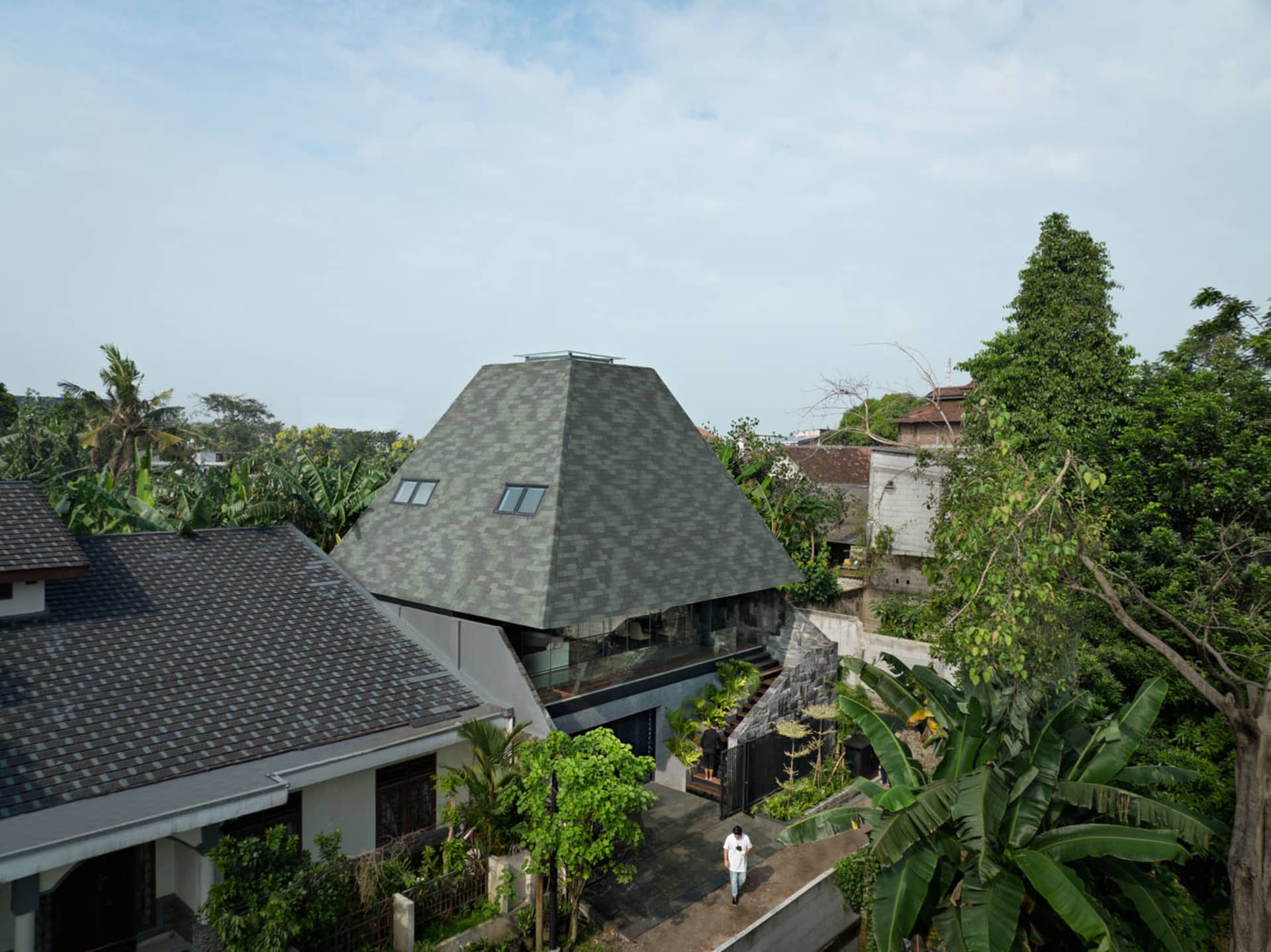 A modern house with a metal-clad roof surrounded by lush greenery.