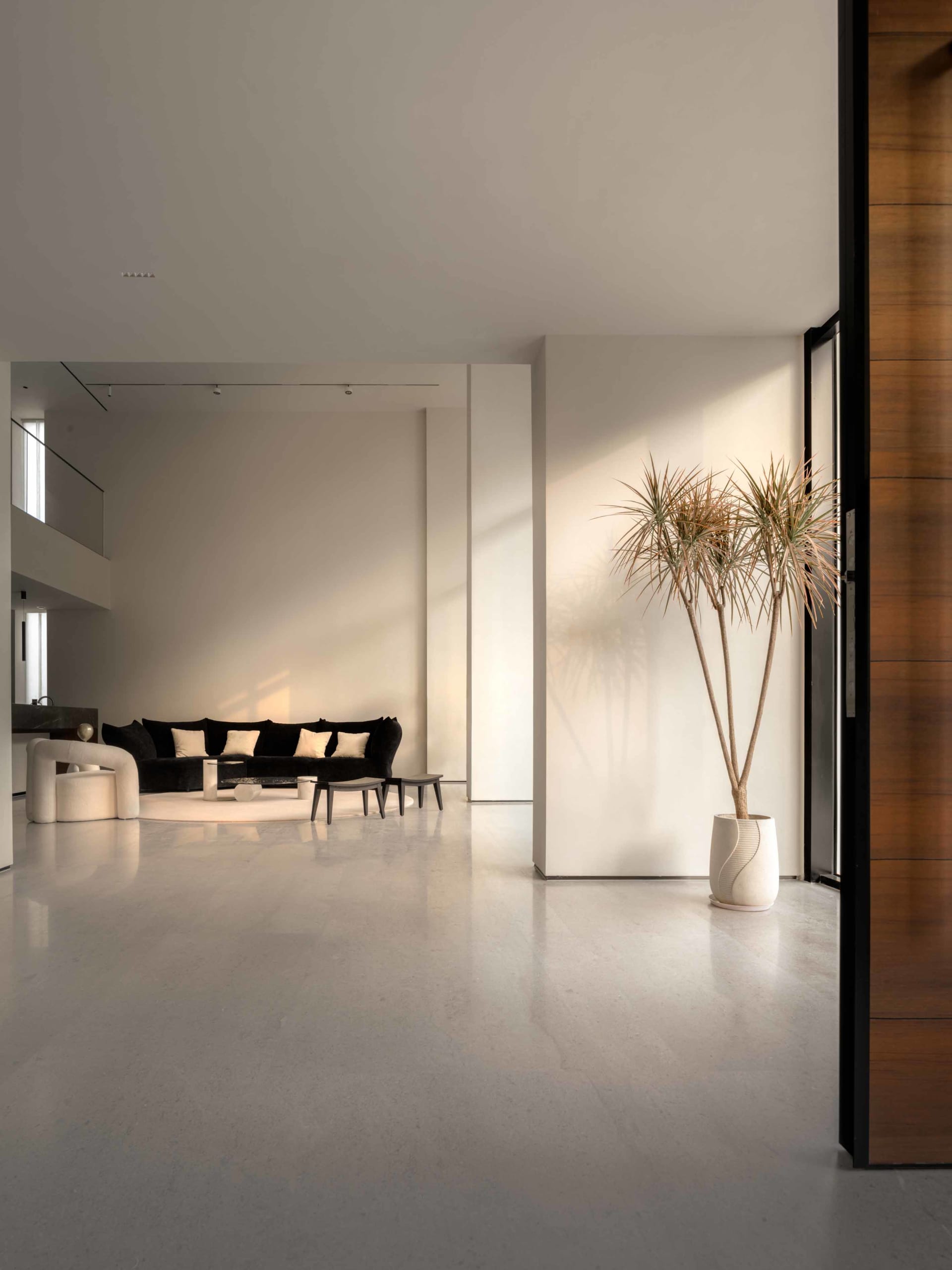 A modern, minimalist living room featuring a concrete floor, white walls, and a black and white color palette.