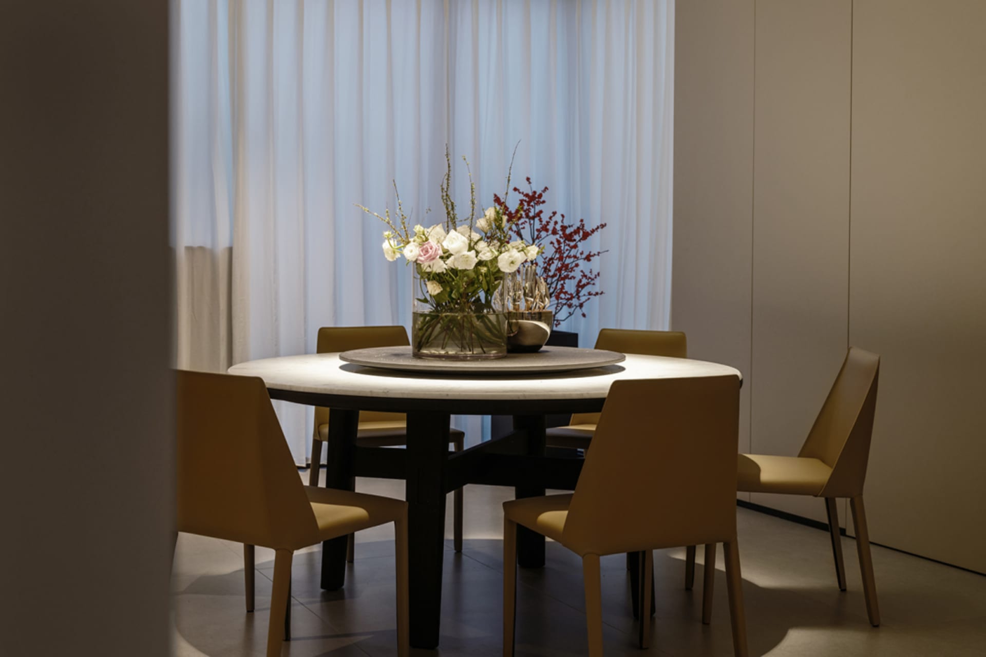 Modern dining room with a round marble table adorned with a floral centerpiece.