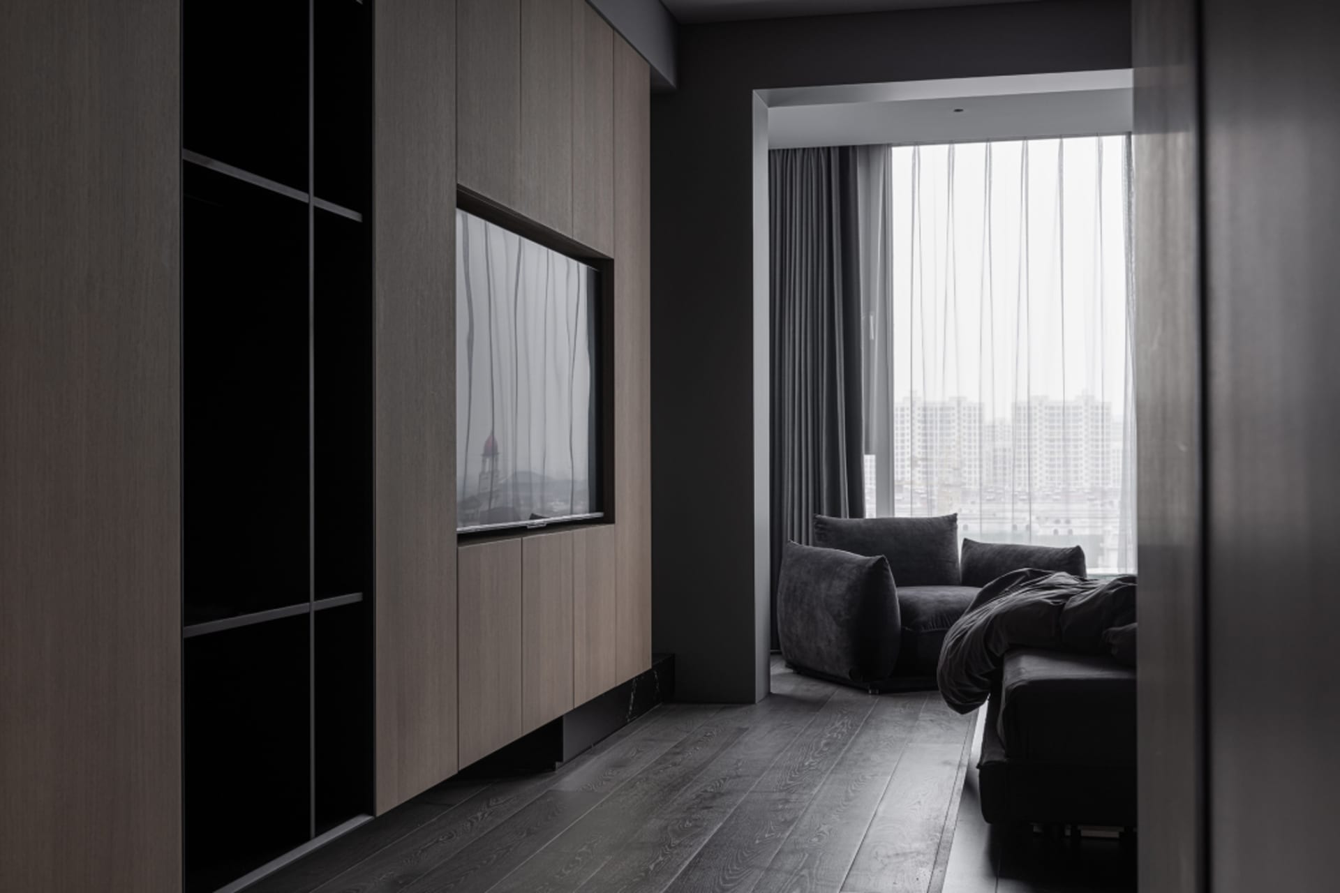 Modern living room with dark wood flooring, dark curtains, and a dark sofa with pillows.