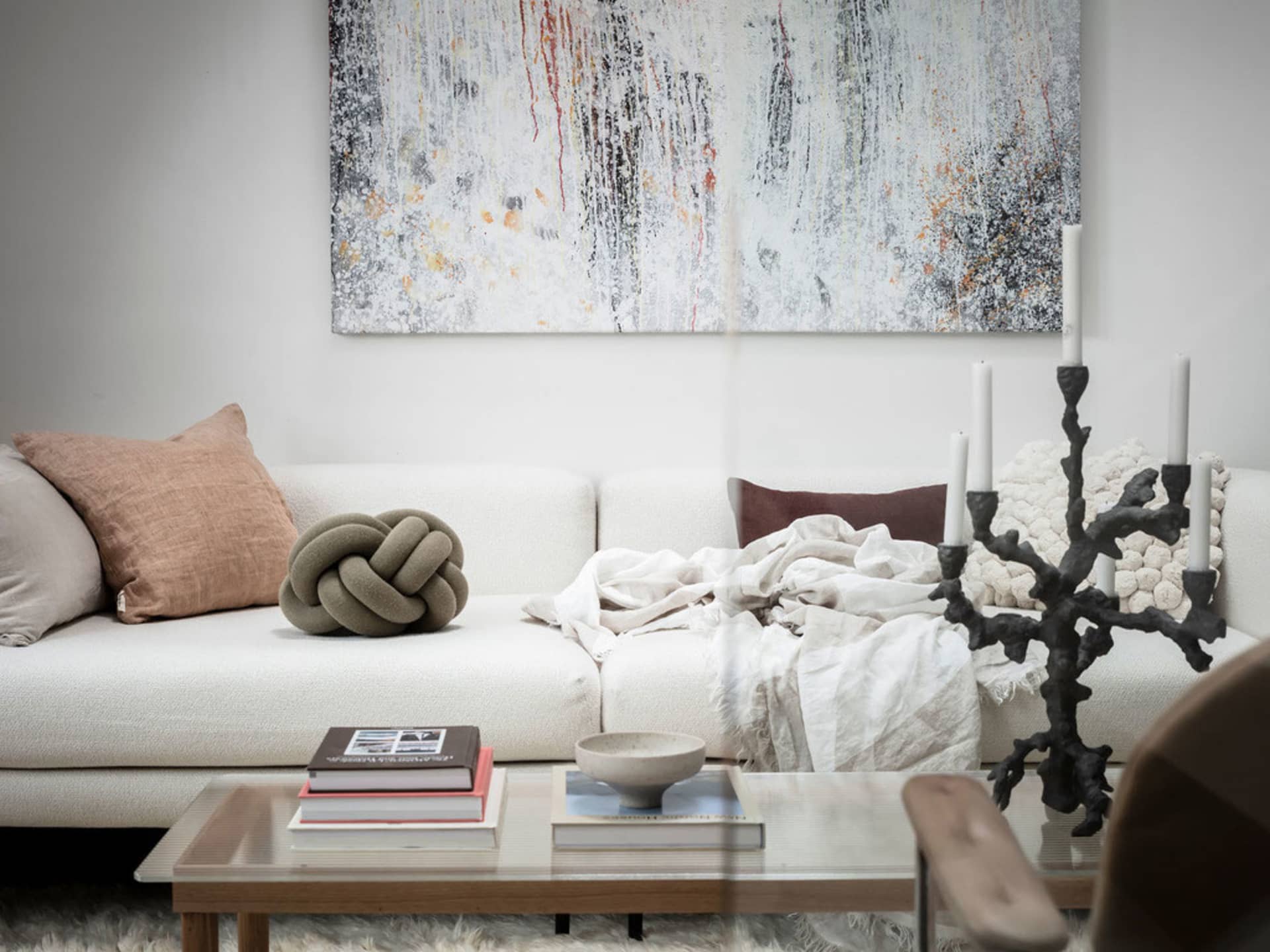A modern living room with a white sofa, abstract painting, wooden coffee table, and concrete floor.
