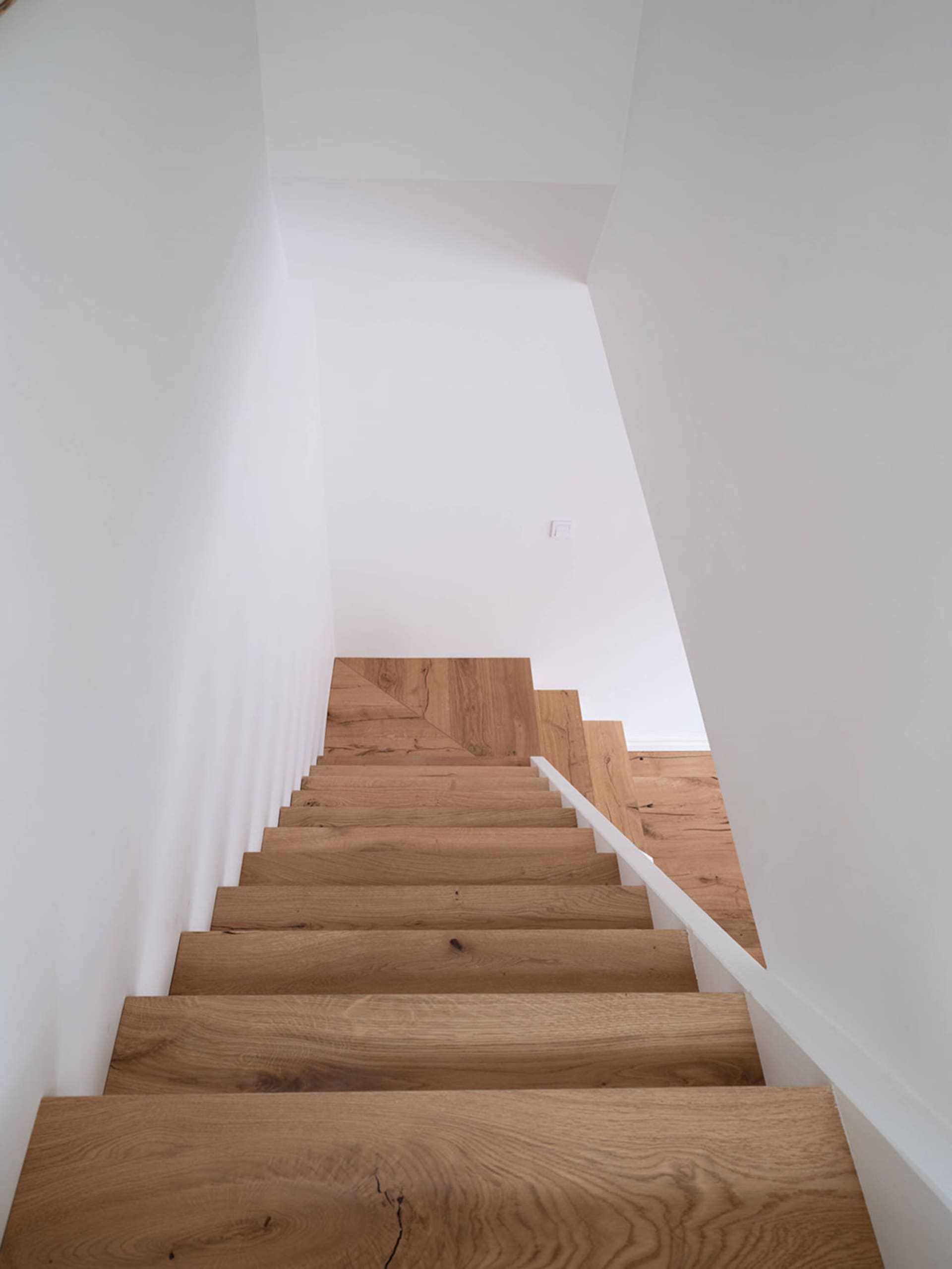 A wooden staircase with white walls and a white handrail leading upwards.