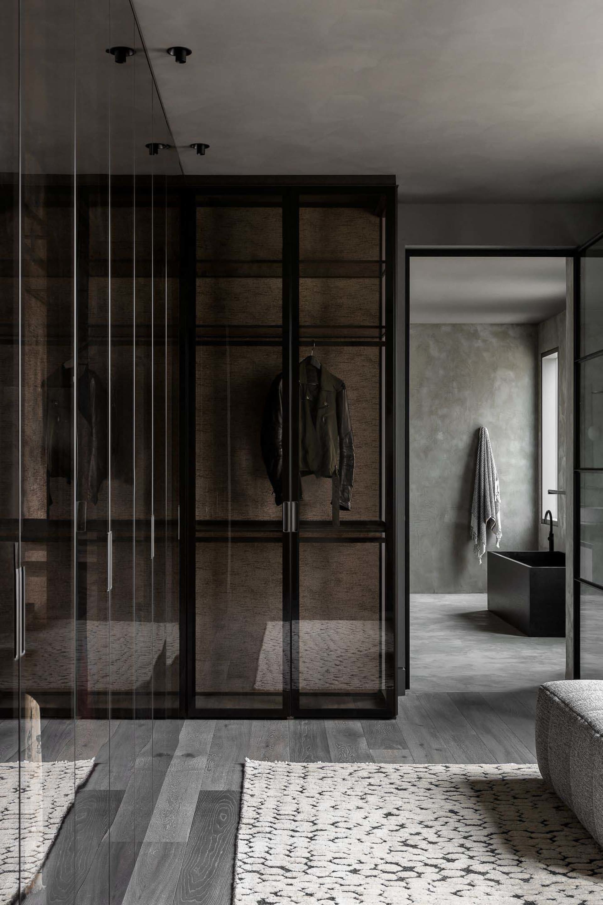 Modern interior design featuring a glass and wood clothes closet with a leather jacket hanging inside.