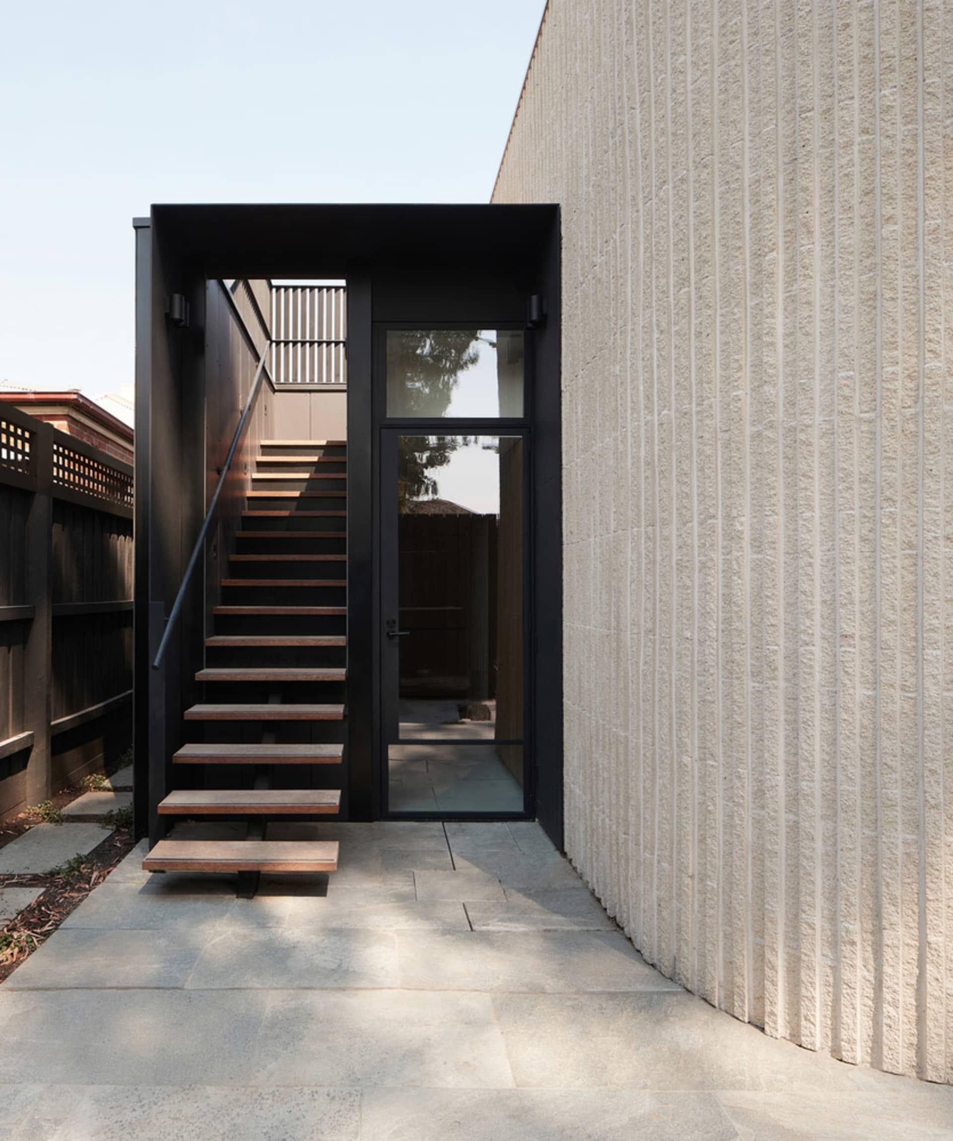 Modern entrance featuring wooden stairs and a concrete wall
