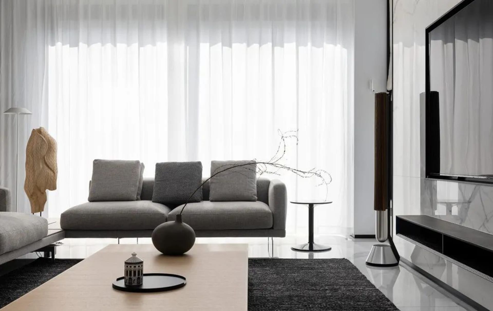 A modern minimalist living room with grey sofa, wooden coffee table, and glass elements