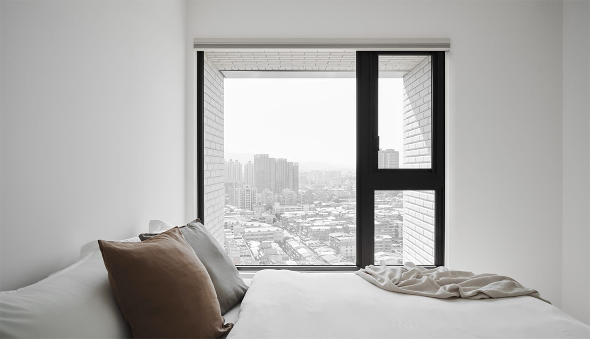 A minimalist bedroom featuring a bed with soft textiles, white brick texture walls, and white walls.