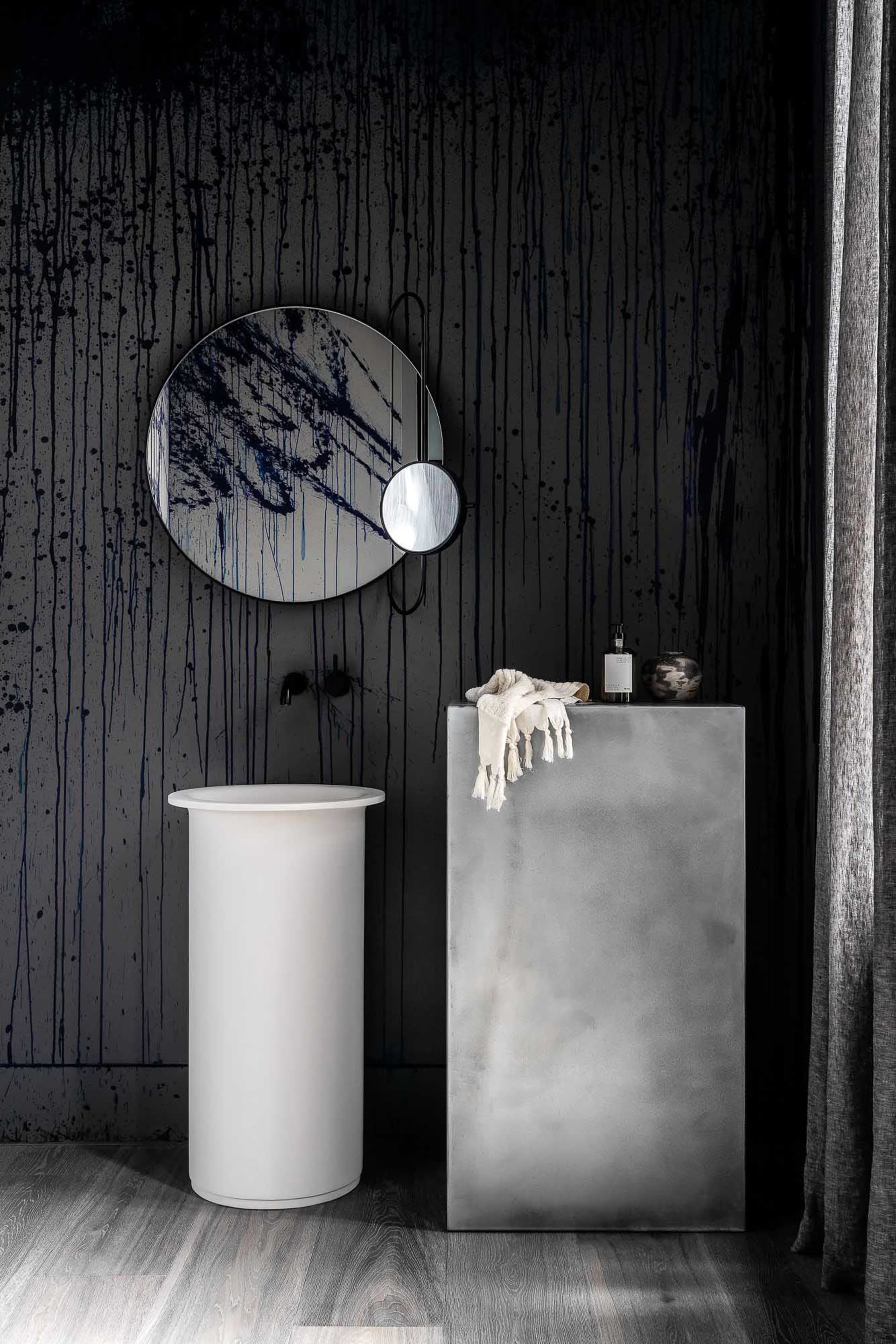 A modern bathroom featuring a minimalist design with concrete walls and a cylindrical pedestal sink.