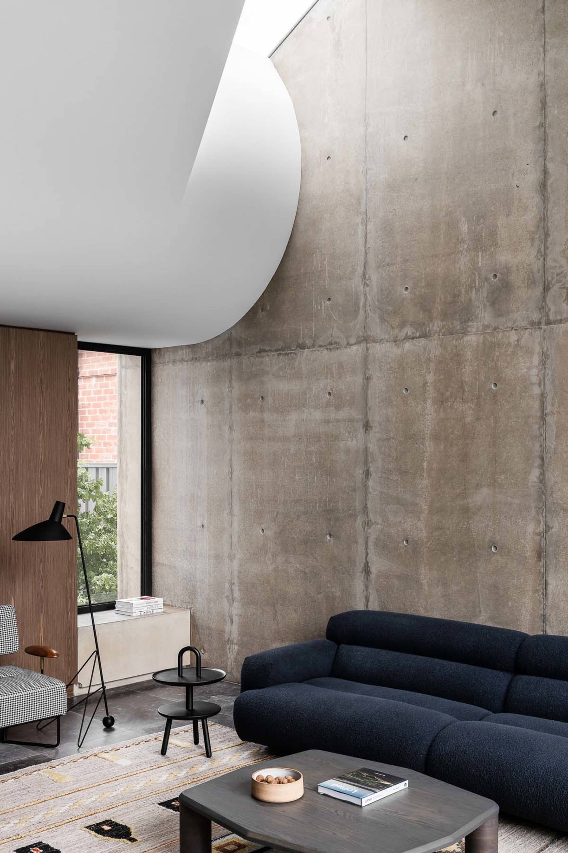 A minimalist living room featuring a concrete wall and floor, with a navy blue sofa and a dark wood coffee table.