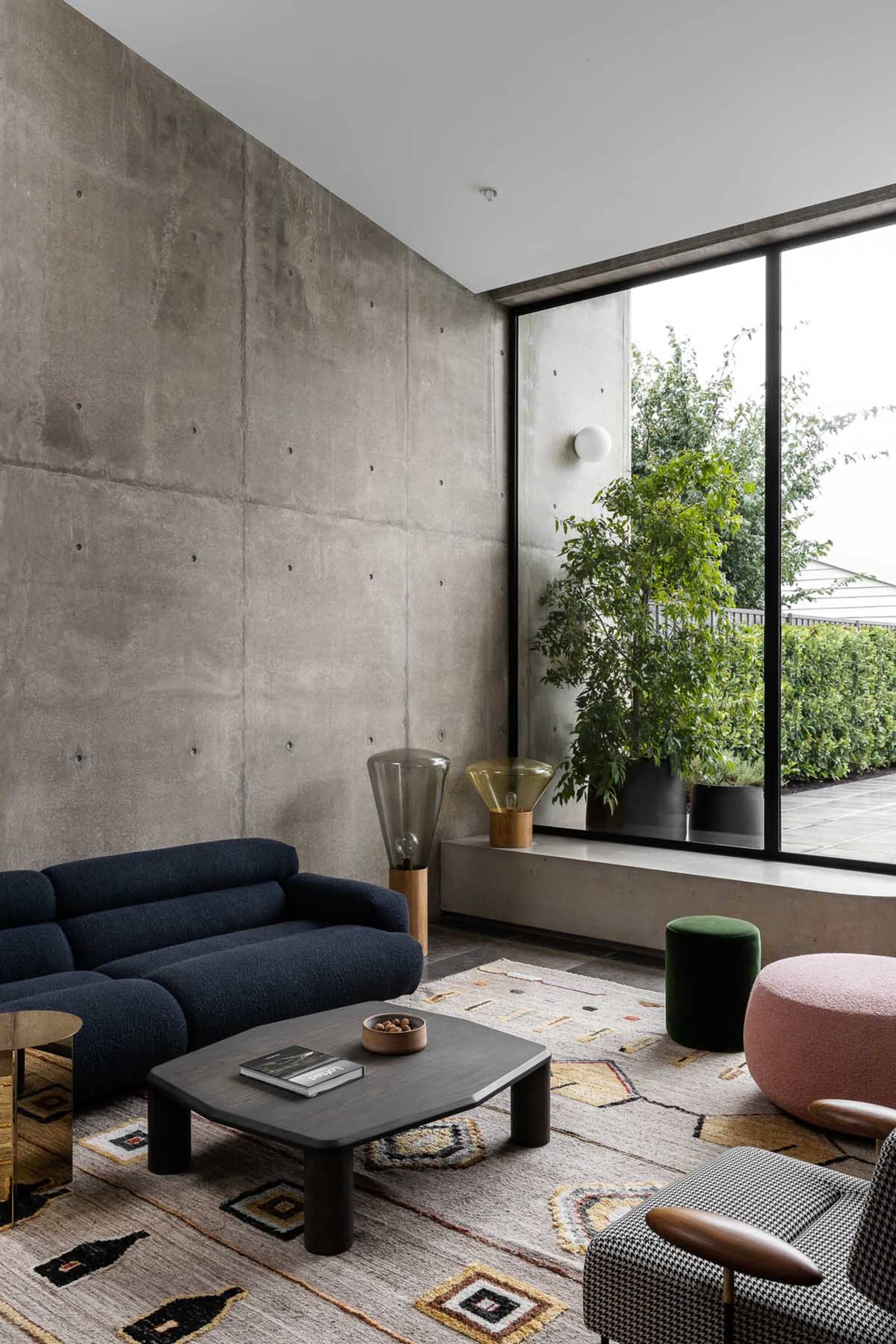 Modern living room with minimalist furniture, concrete walls, and large window.