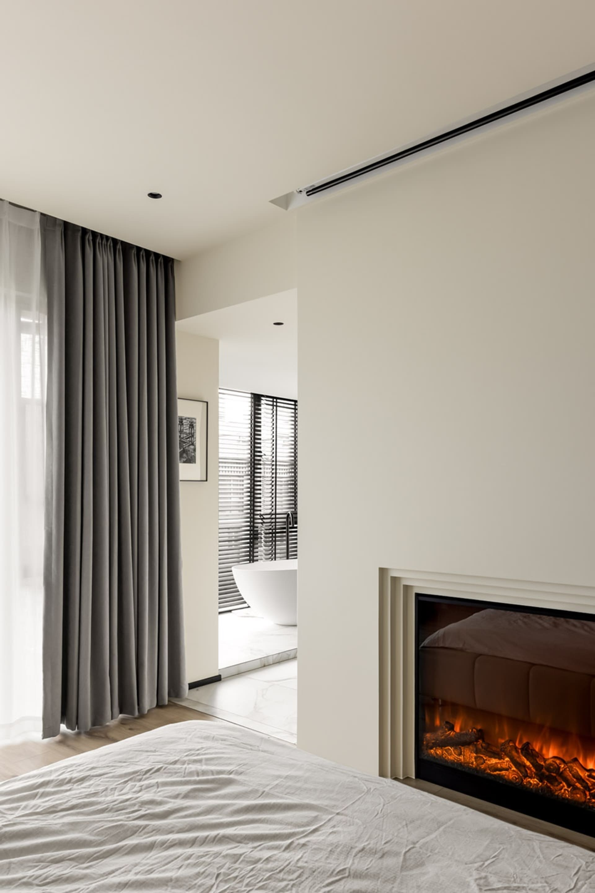 Modern minimalist bedroom with white walls, a bed, a fireplace, and a bathroom visible through an open doorway.