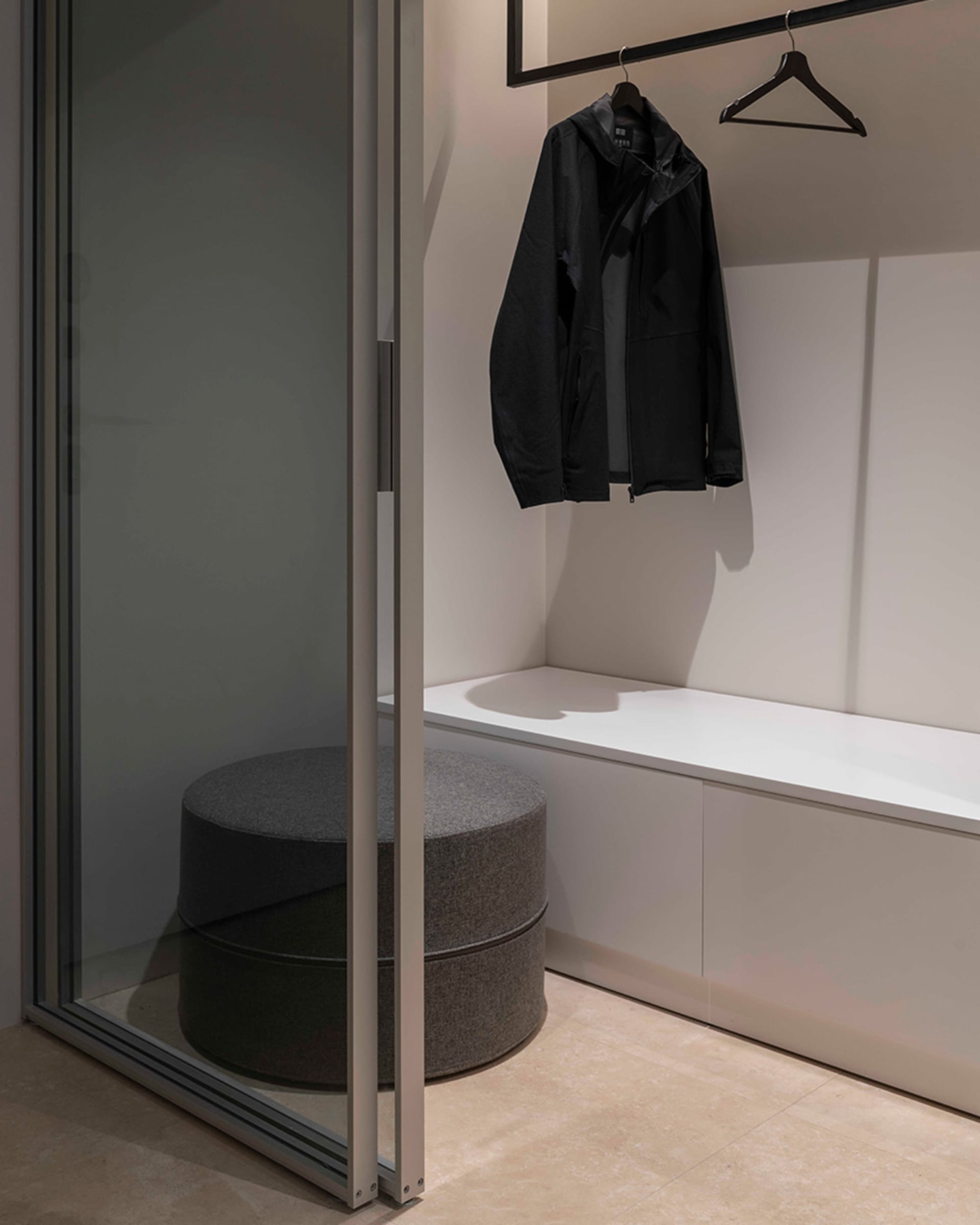 A modern minimalist closet with a glass sliding door, a white counter, and a black jacket hanging on a black hanger.