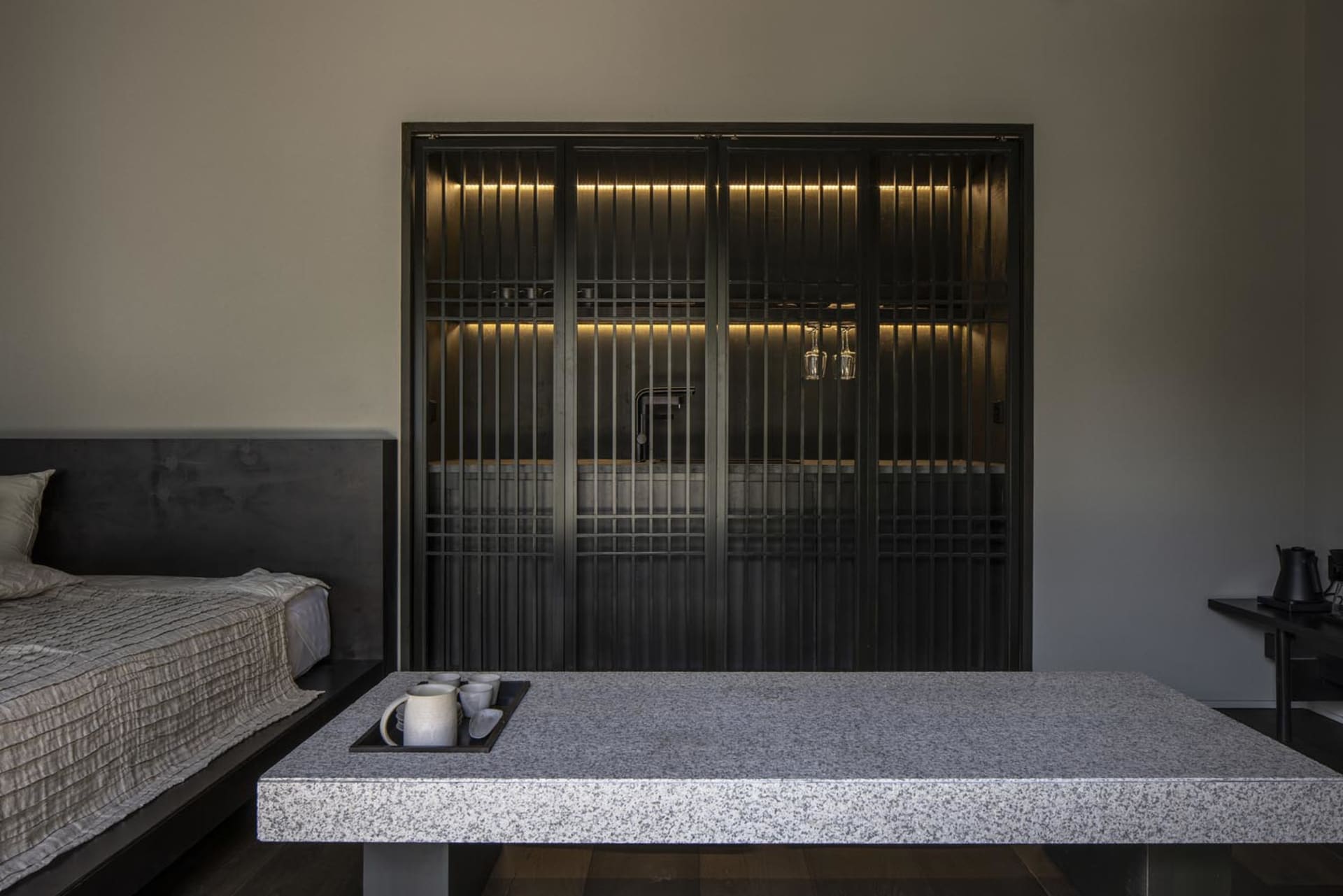 A minimalist bedroom featuring a granite table with a tray holding a small arrangement of coffee cups and mugs.
