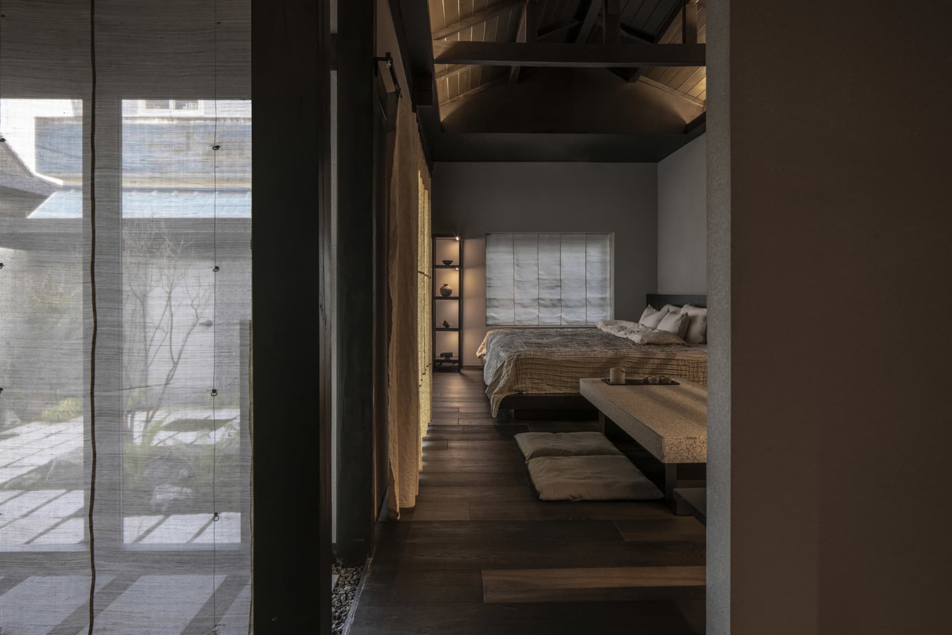 A minimalist bedroom with a wooden floor, a bed with simple bedding, and a low bench for seating.