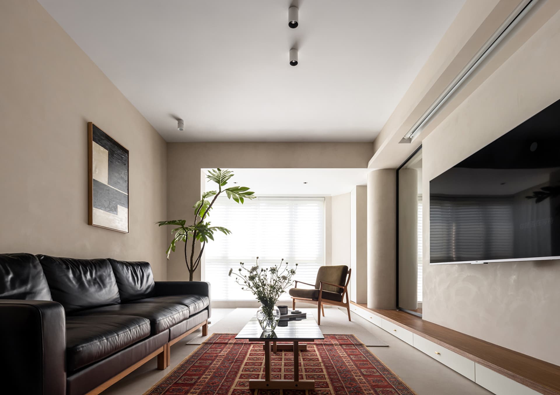 A modern residential living room with a black leather sofa, wooden armchair, and wooden coffee table on a red and brown patte