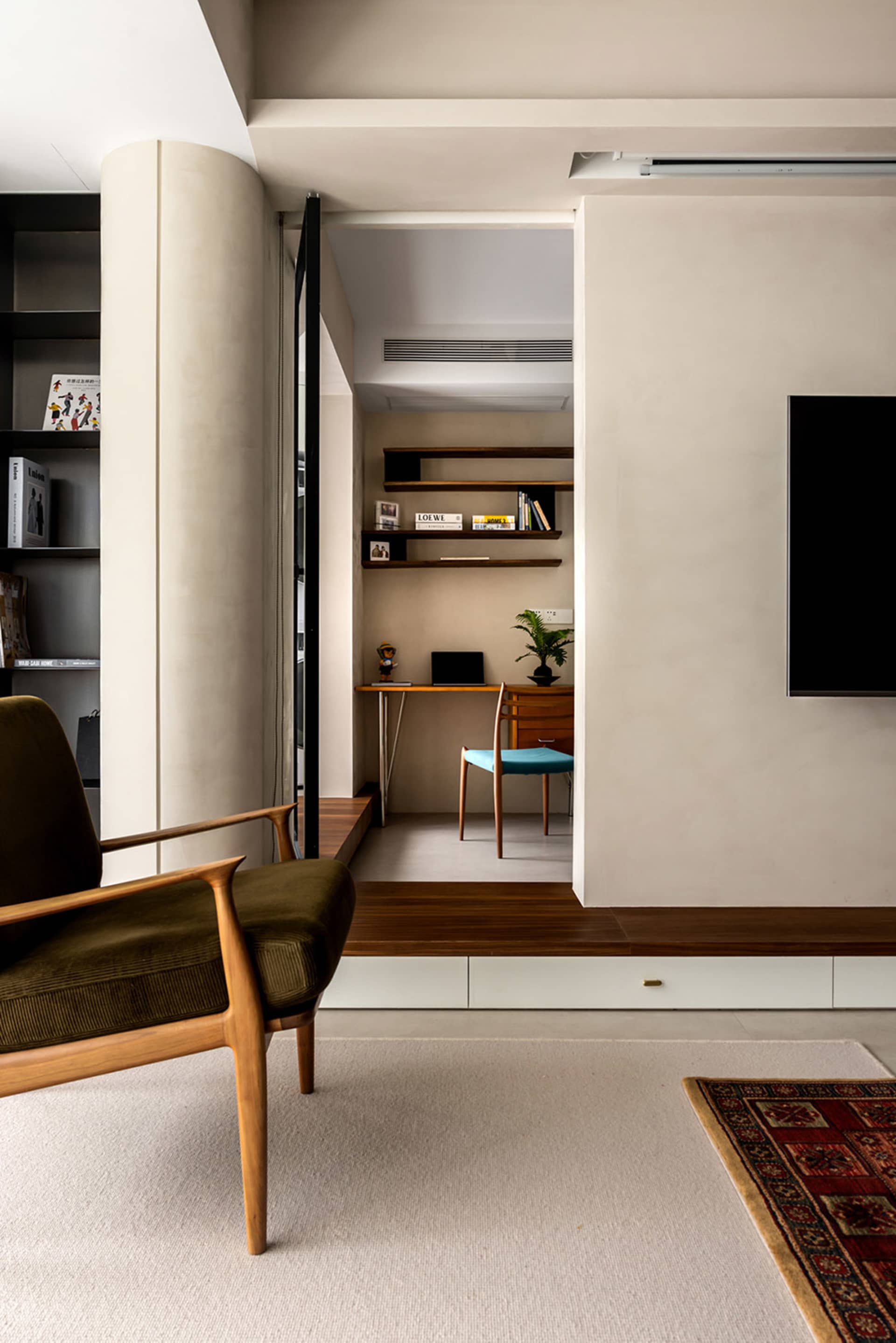 A modern minimalist living room and office space with a wooden chair, concrete floors, and floating shelves.