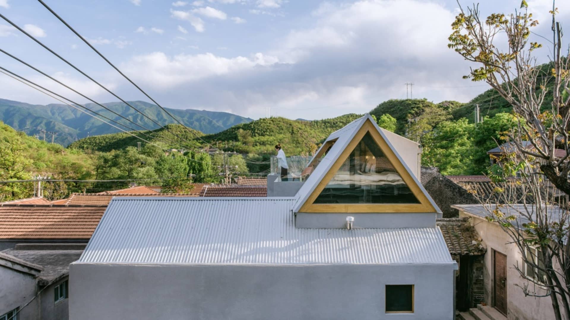 A modern house with a metallic roof and a large glass triangle window.