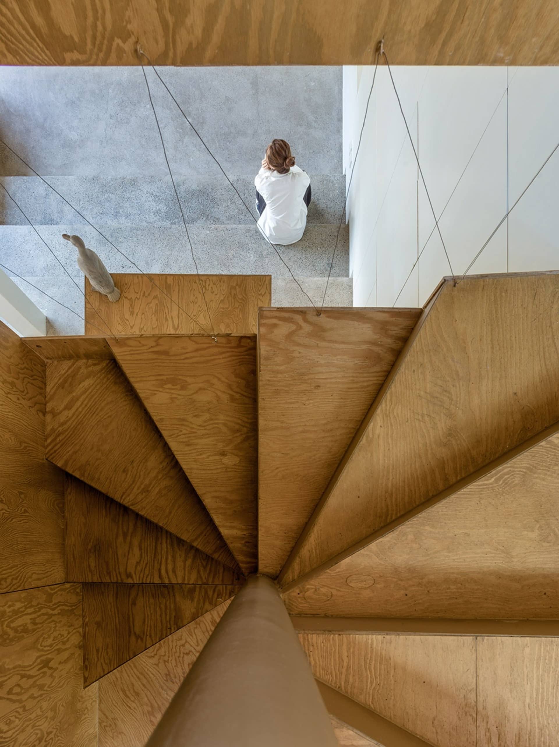 Modern wooden staircase with a person sitting on the steps and a bird sculpture.