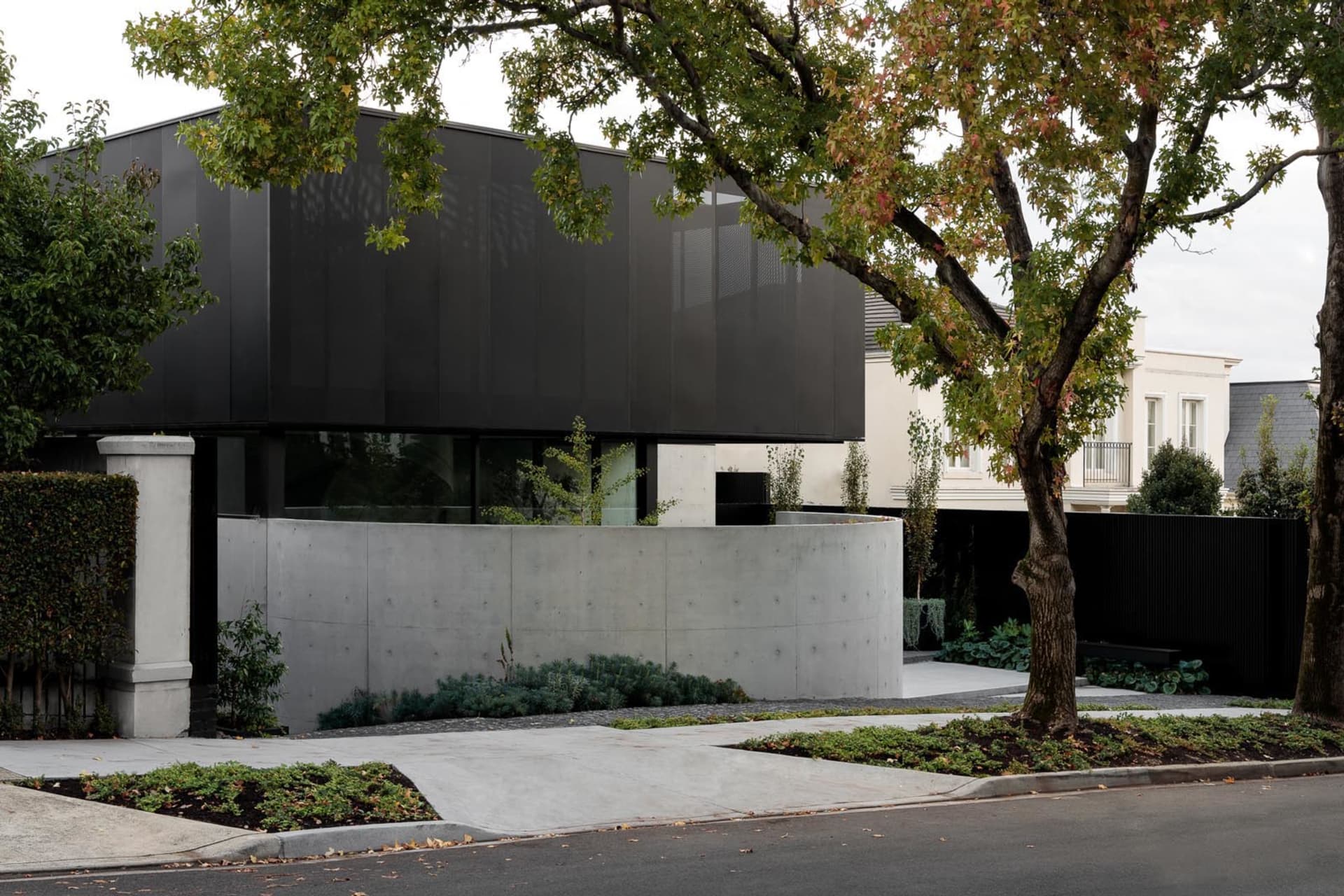 Modern black concrete residential exterior with glass windows and a concrete driveway.