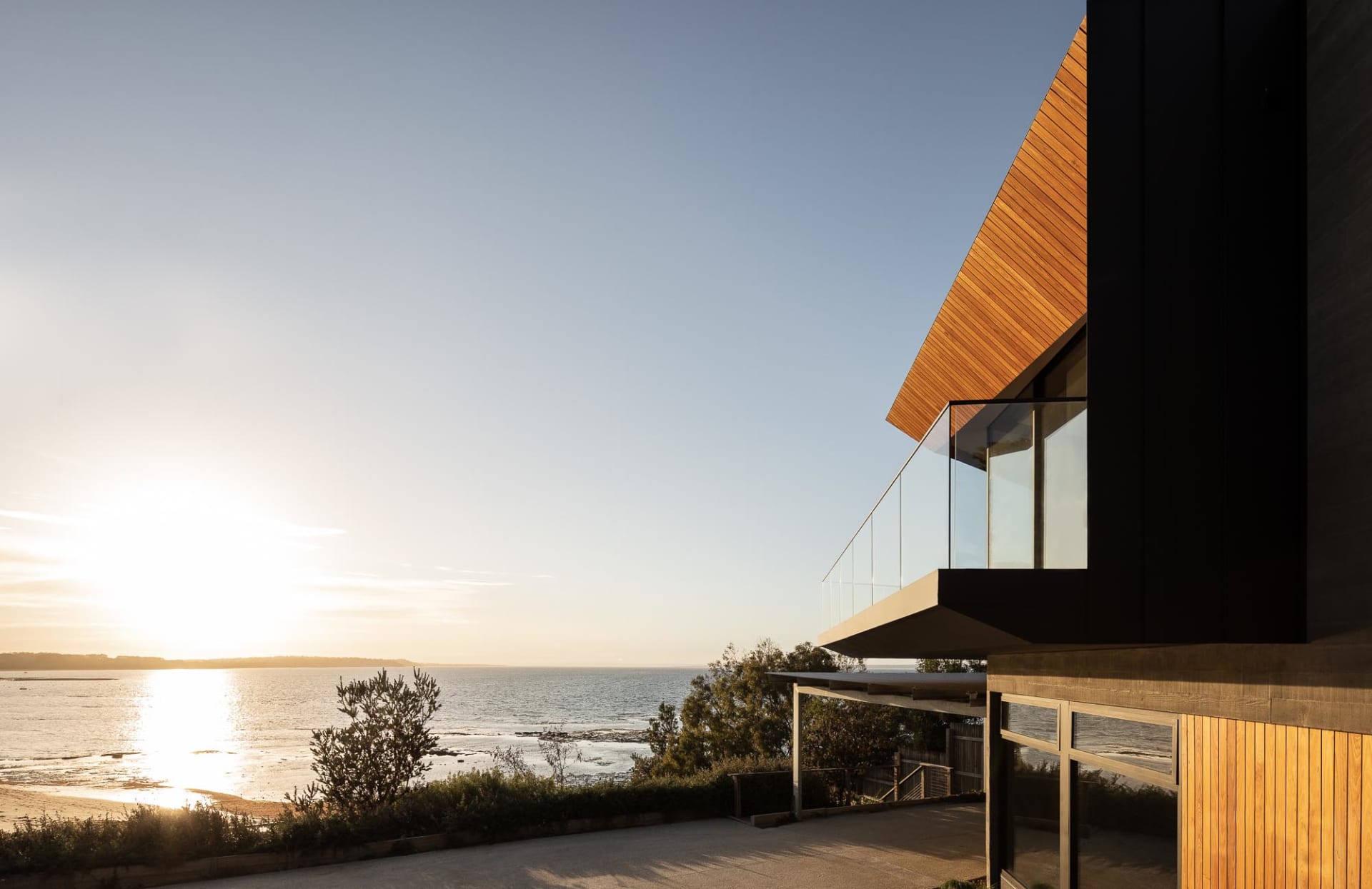 A modern seaside residential property featuring wooden cladding and large glass windows overlooking the ocean.