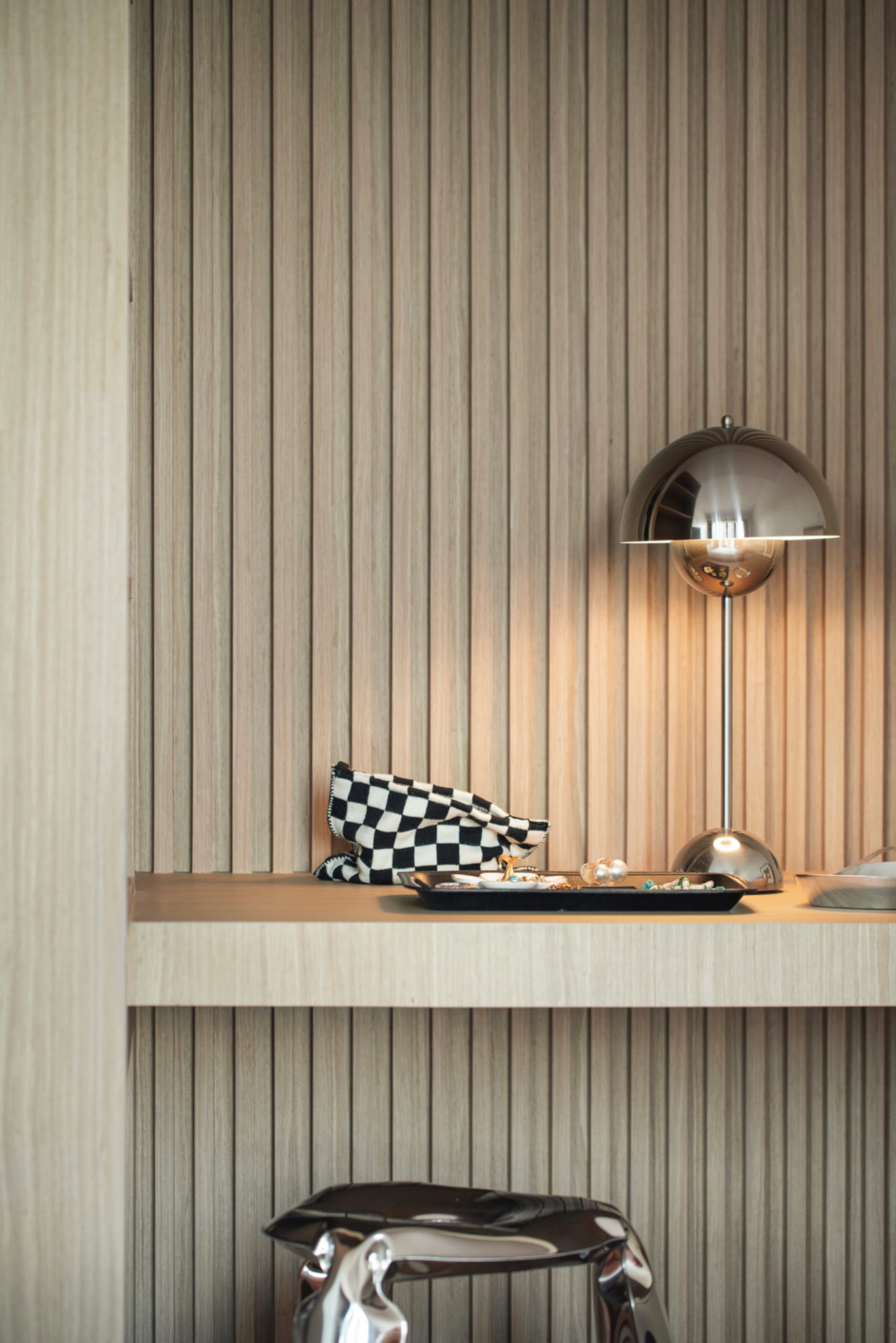 A display of modern accessories on a wooden ledge, featuring a sleek lamp and a checkerboard-patterned pouch.