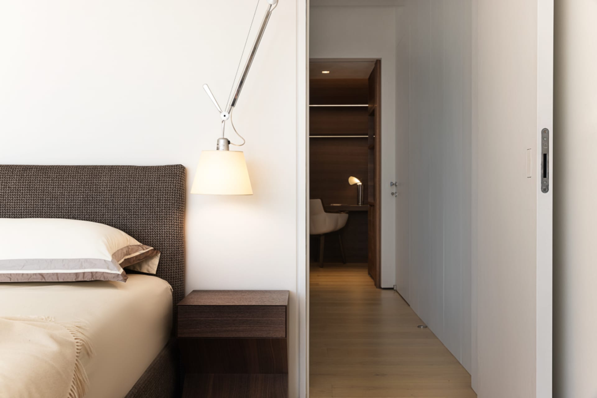 A modern minimalist bedroom with a wooden floor and a bed covered in fabric.