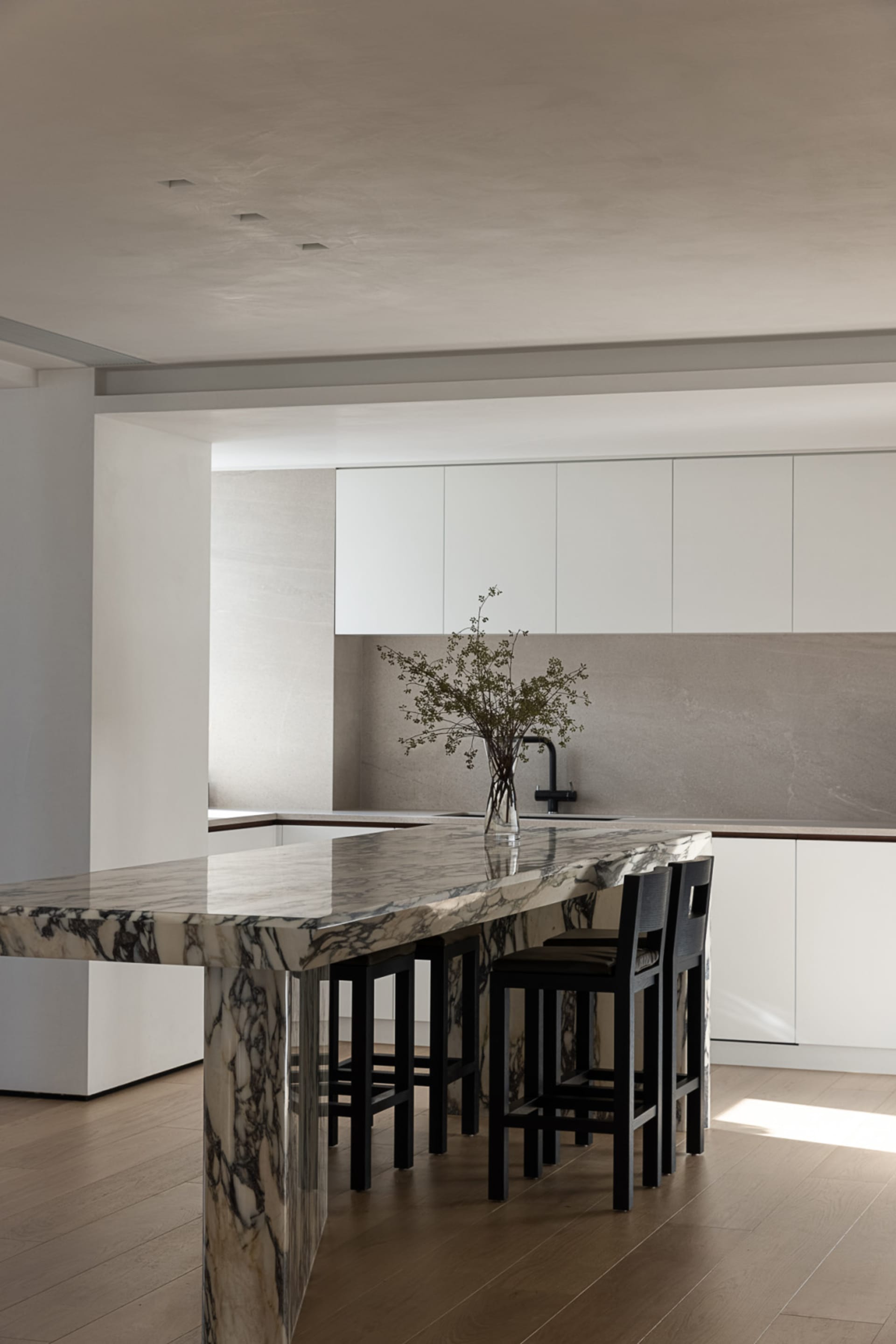 Modern minimalist kitchen with marble countertops and black stools.