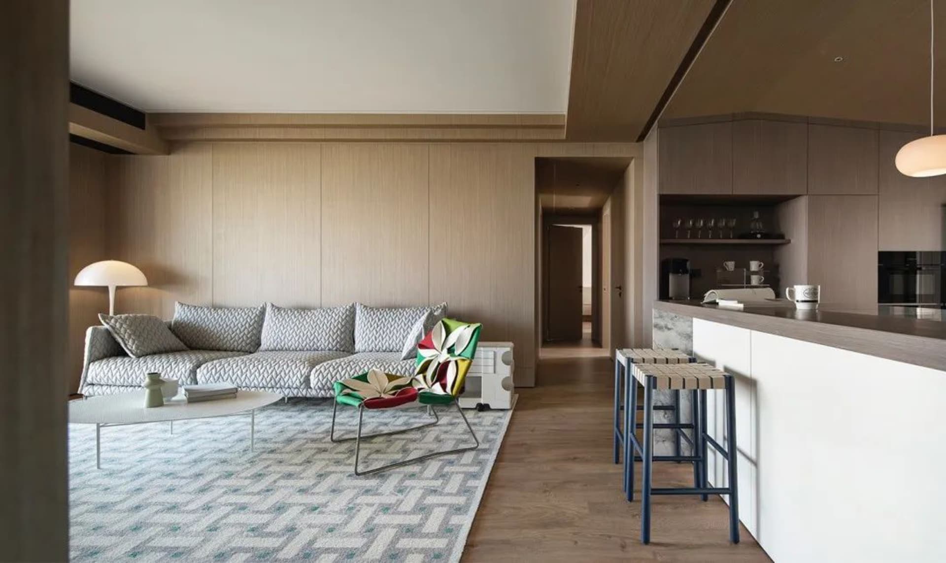 Modern living room with wooden walls and a comfortable seating area, featuring a patterned rug and colorful chairs.