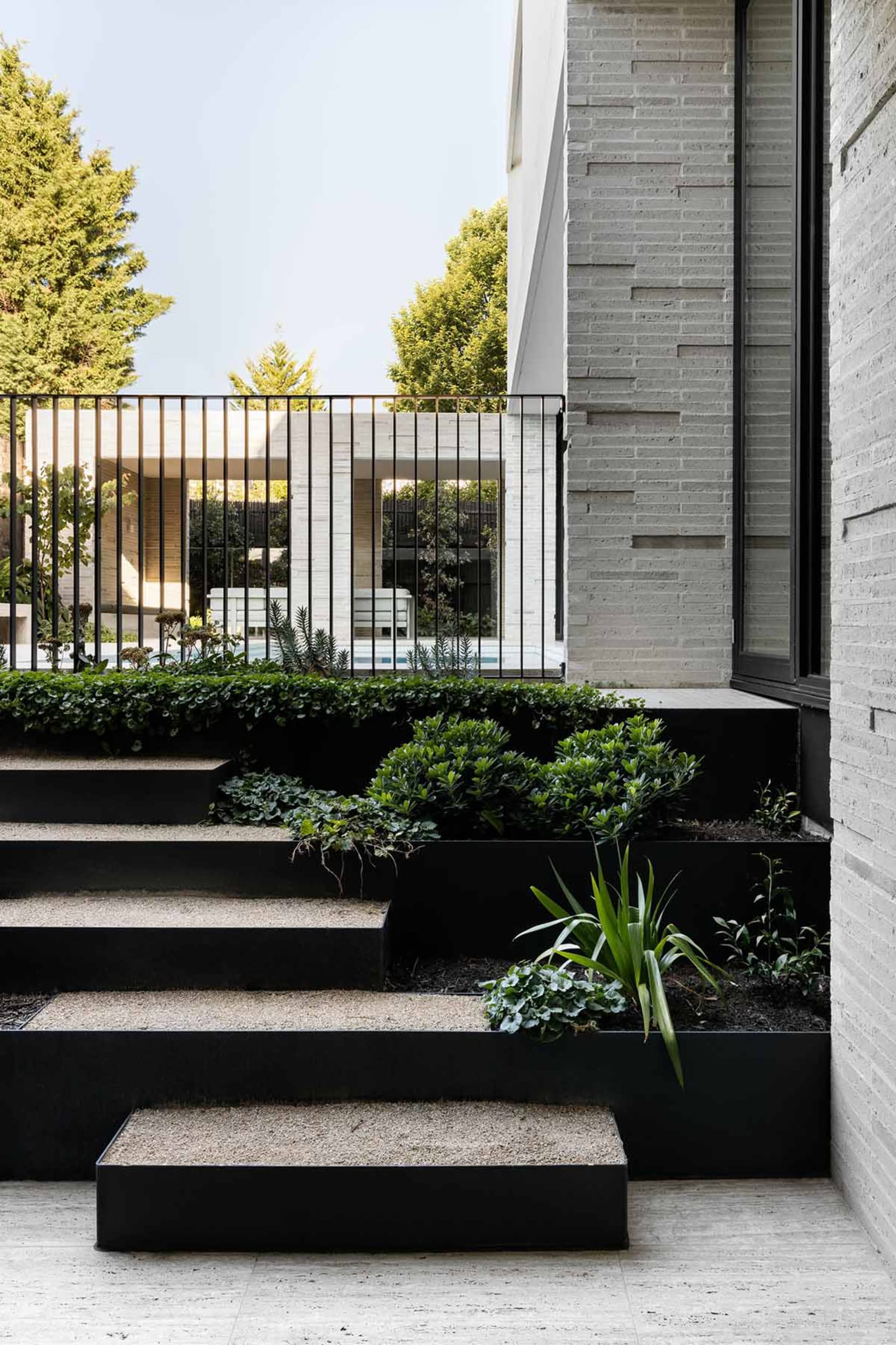 A modern exterior residential entryway with concrete stairs and steel railings, featuring a landscaped garden