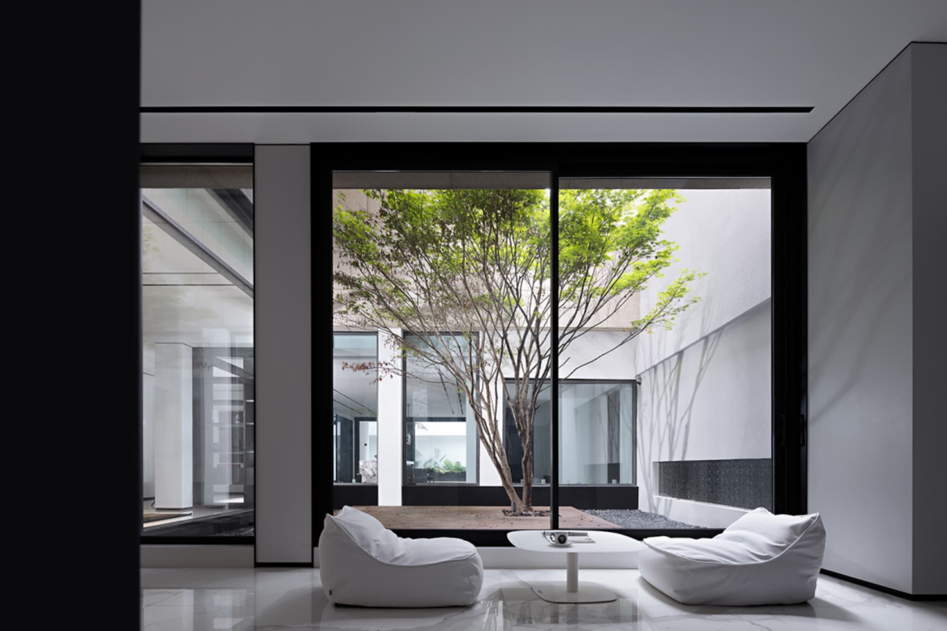 A minimalist modern living room with glass windows and white furniture.