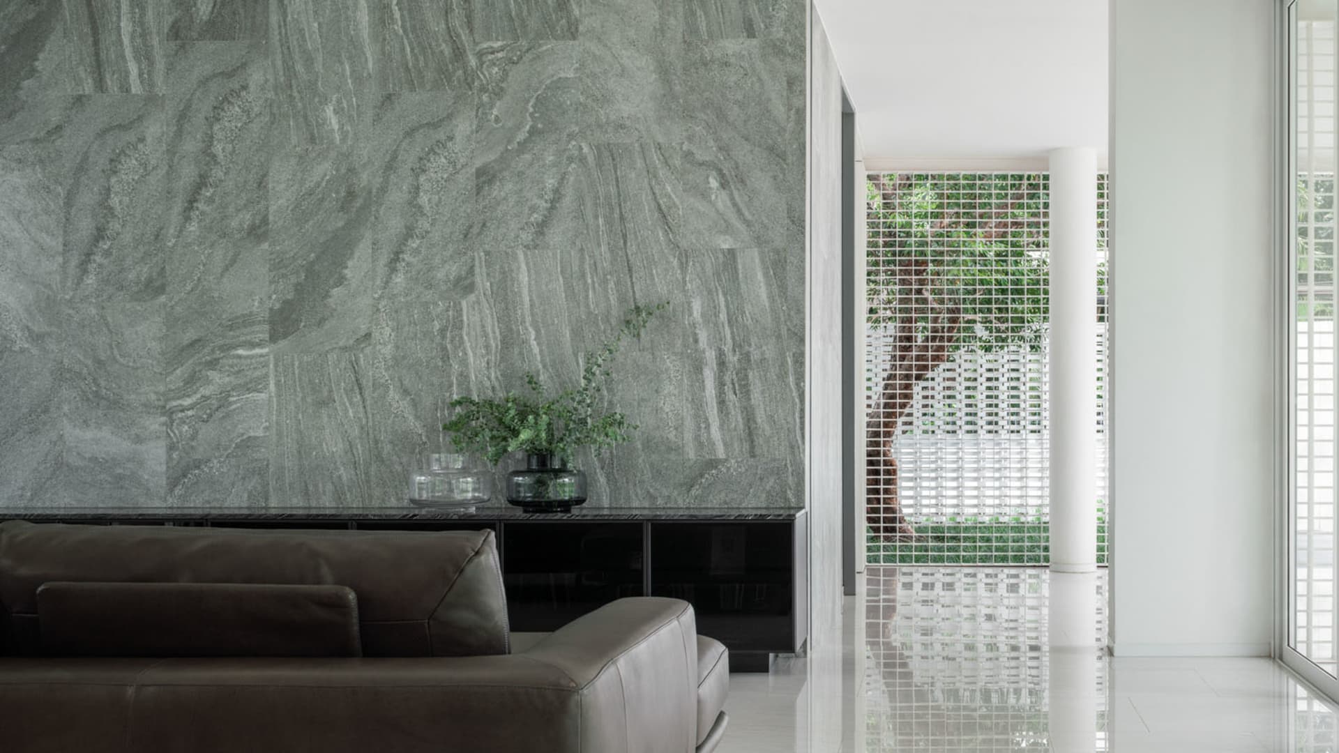 Modern living room with marble walls, white floors, and a brown leather sofa.