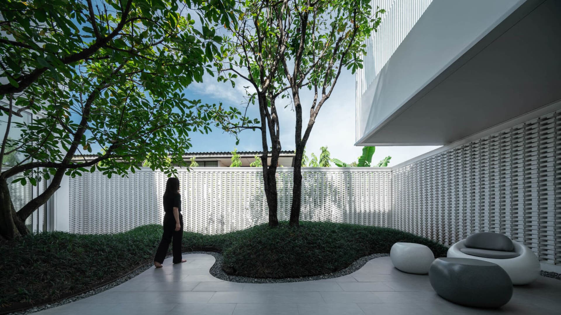 A modern, open-concept residential space featuring concrete floors, glass walls, and lush greenery.