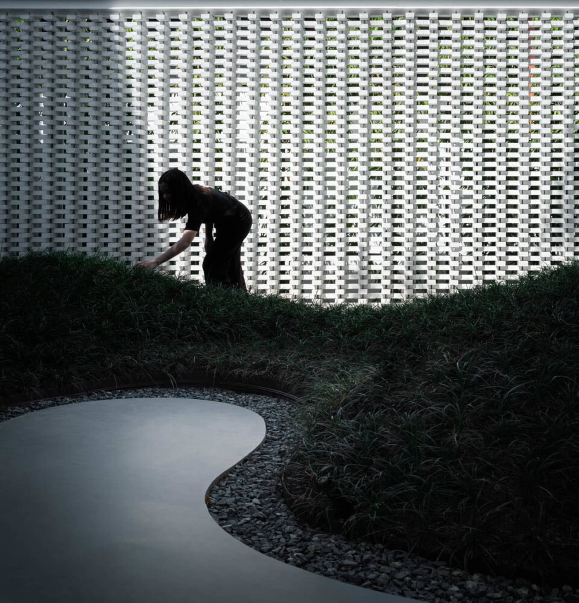 A minimalist garden featuring a curved concrete path surrounded by greenery and gravel.