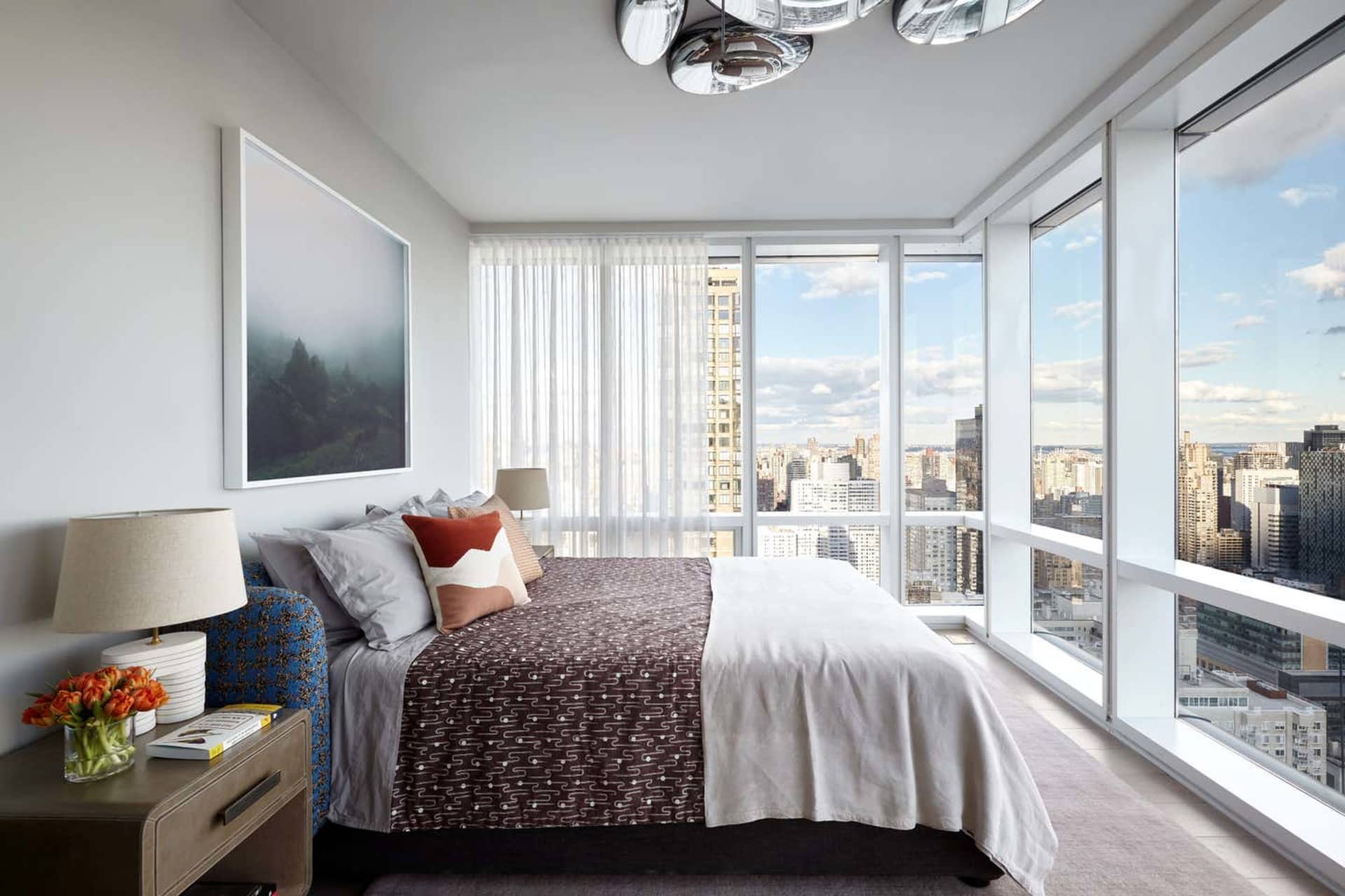 A modern bedroom featuring contemporary textiles, glass window frames, and a city view.