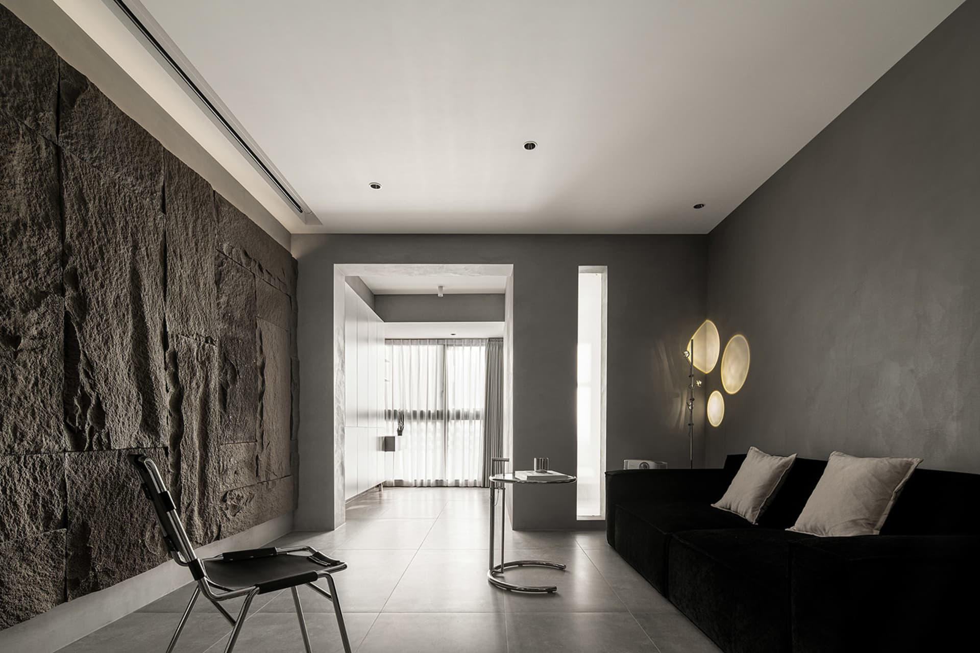 A minimalist residential interior featuring polished concrete walls, a black sofa, and modern lighting.