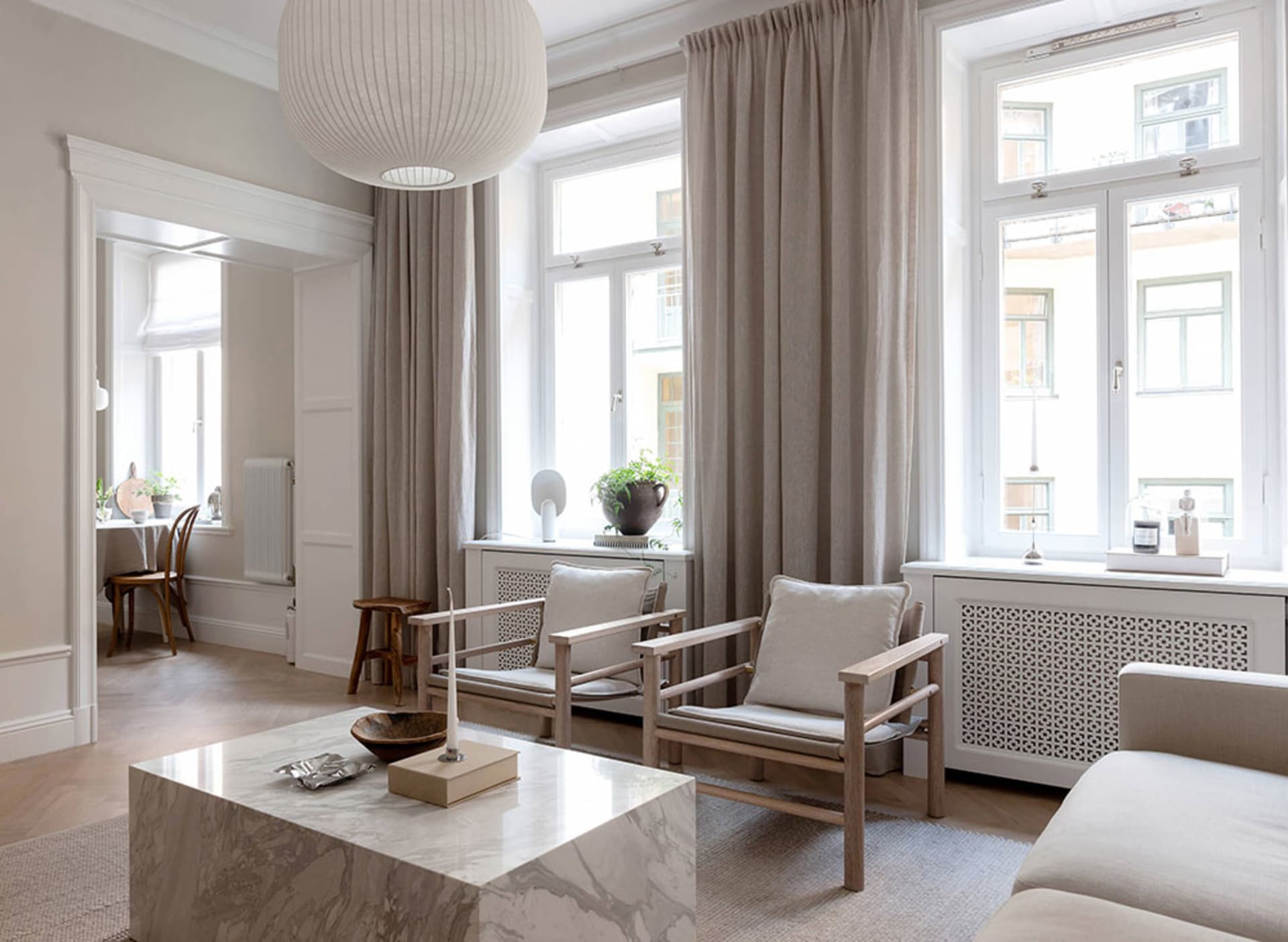 A minimalist living room with neutral-toned furniture and decor, featuring a white marble coffee table, wooden chairs, and la