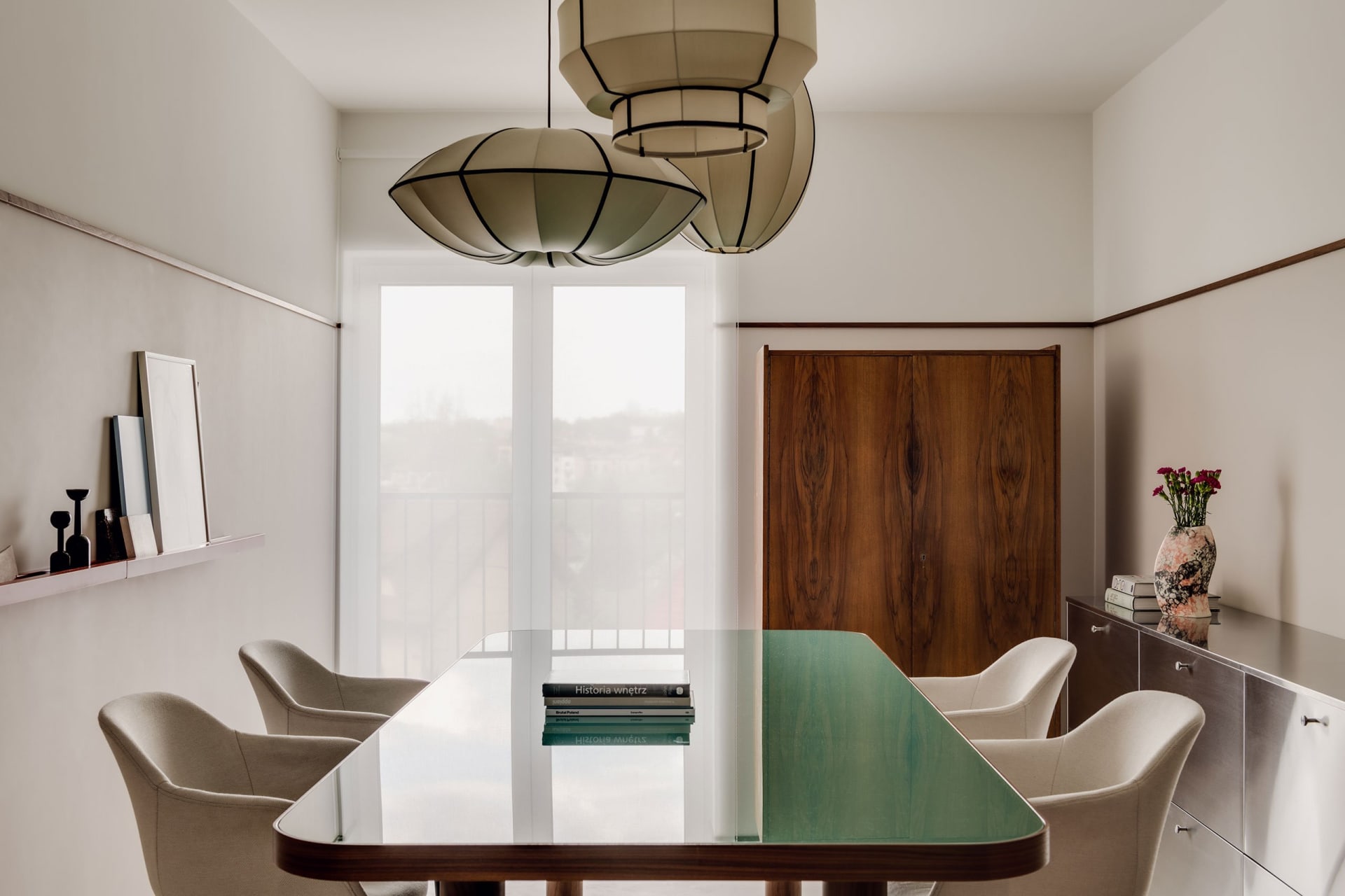 A contemporary dining room with a glass table, wooden cabinet, and fabric chairs.