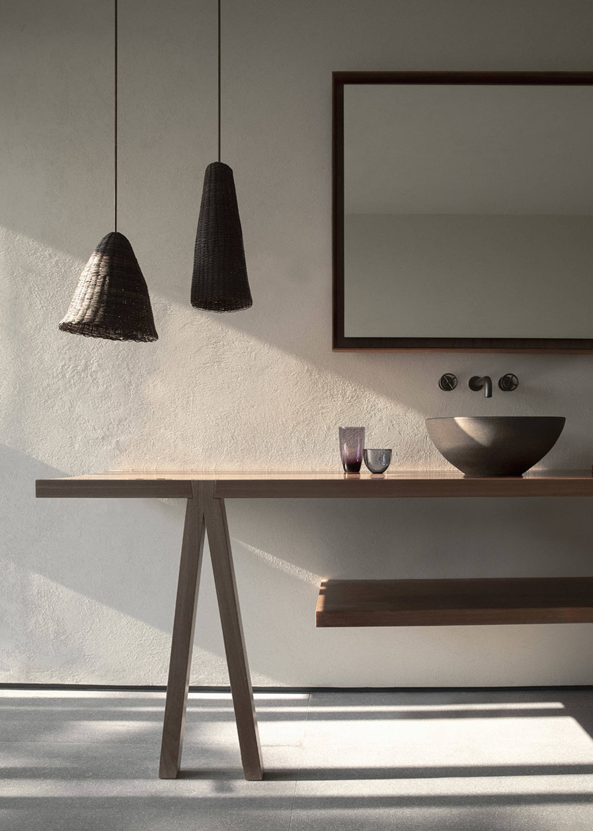 A modern minimalist bathroom with a wooden table and floating shelves, a black woven pendant light, and a sink with a bowl-sh