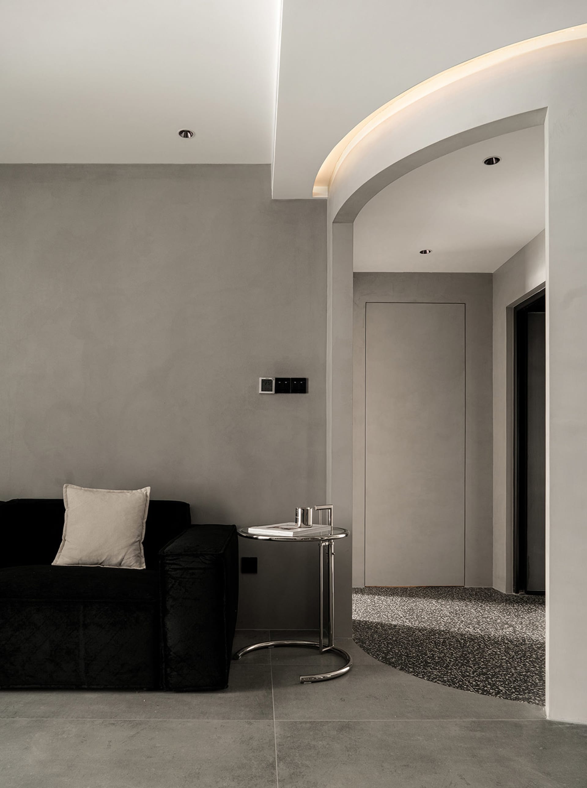 A modern minimalist living room with concrete walls, metal accents, and an entryway
