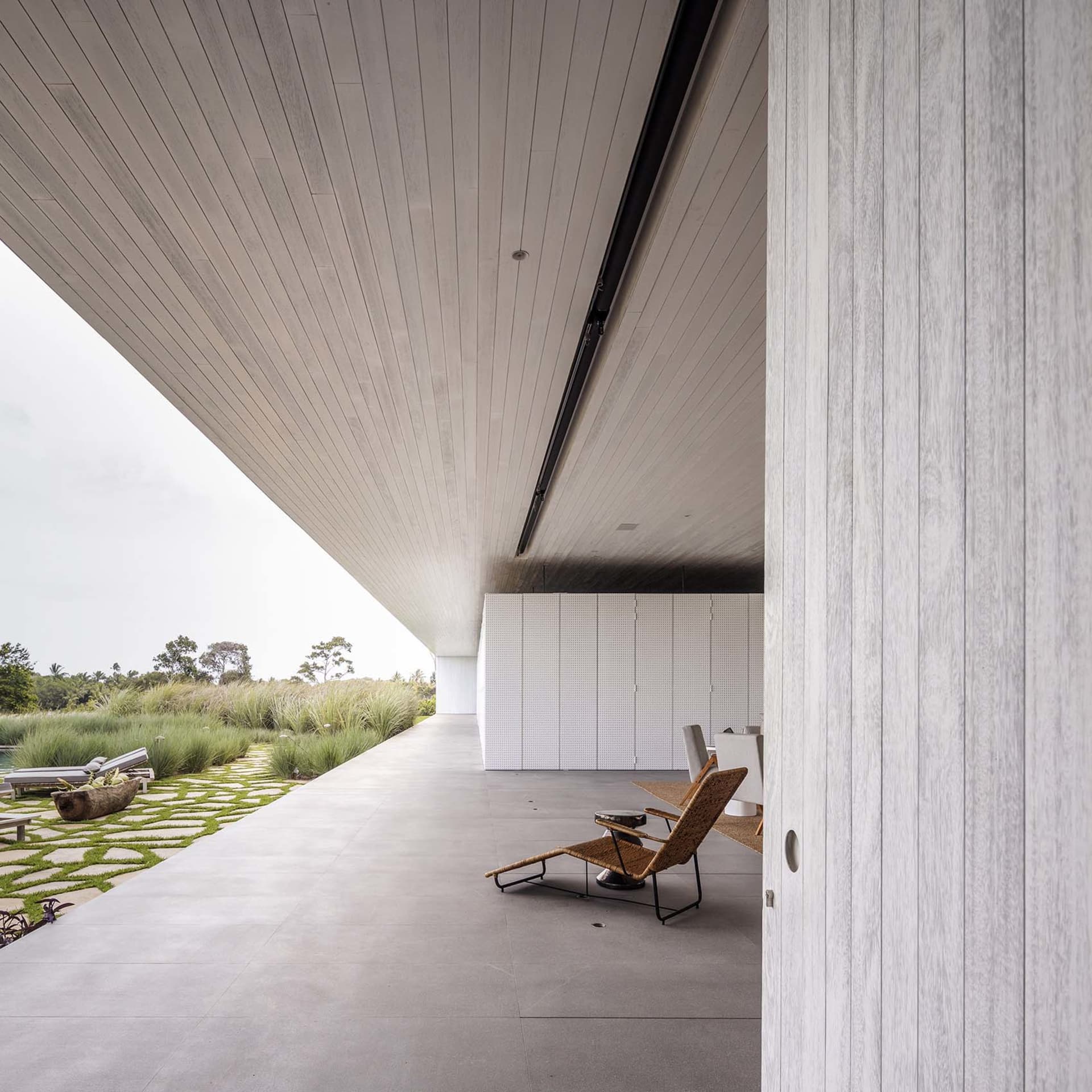 An image of a minimalist, modern residential outdoor space with a concrete floor and walls, featuring a single natural woven
