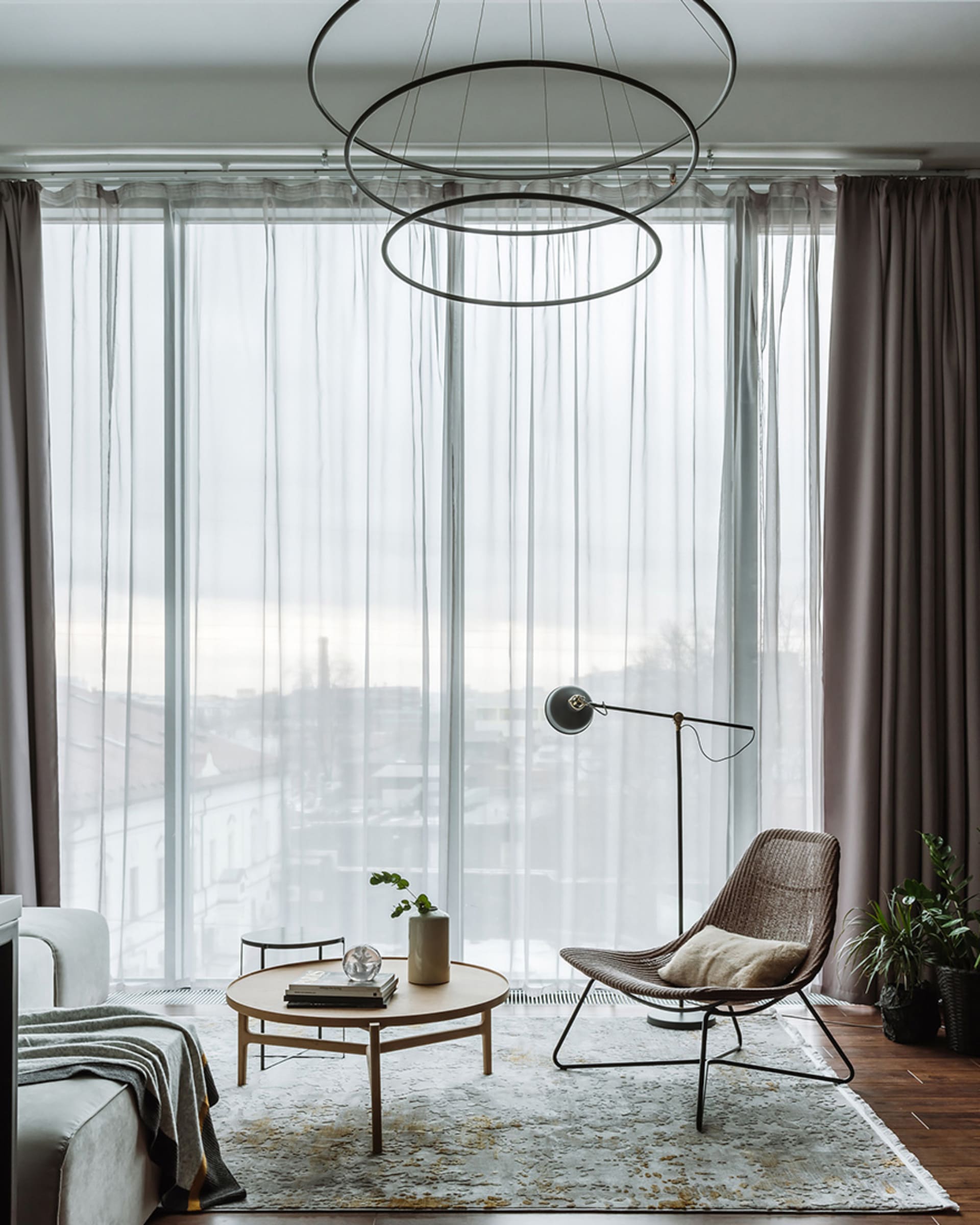 A modern minimalist living room with transparent curtains, a round wooden coffee table, a floor lamp, and a potted plant.