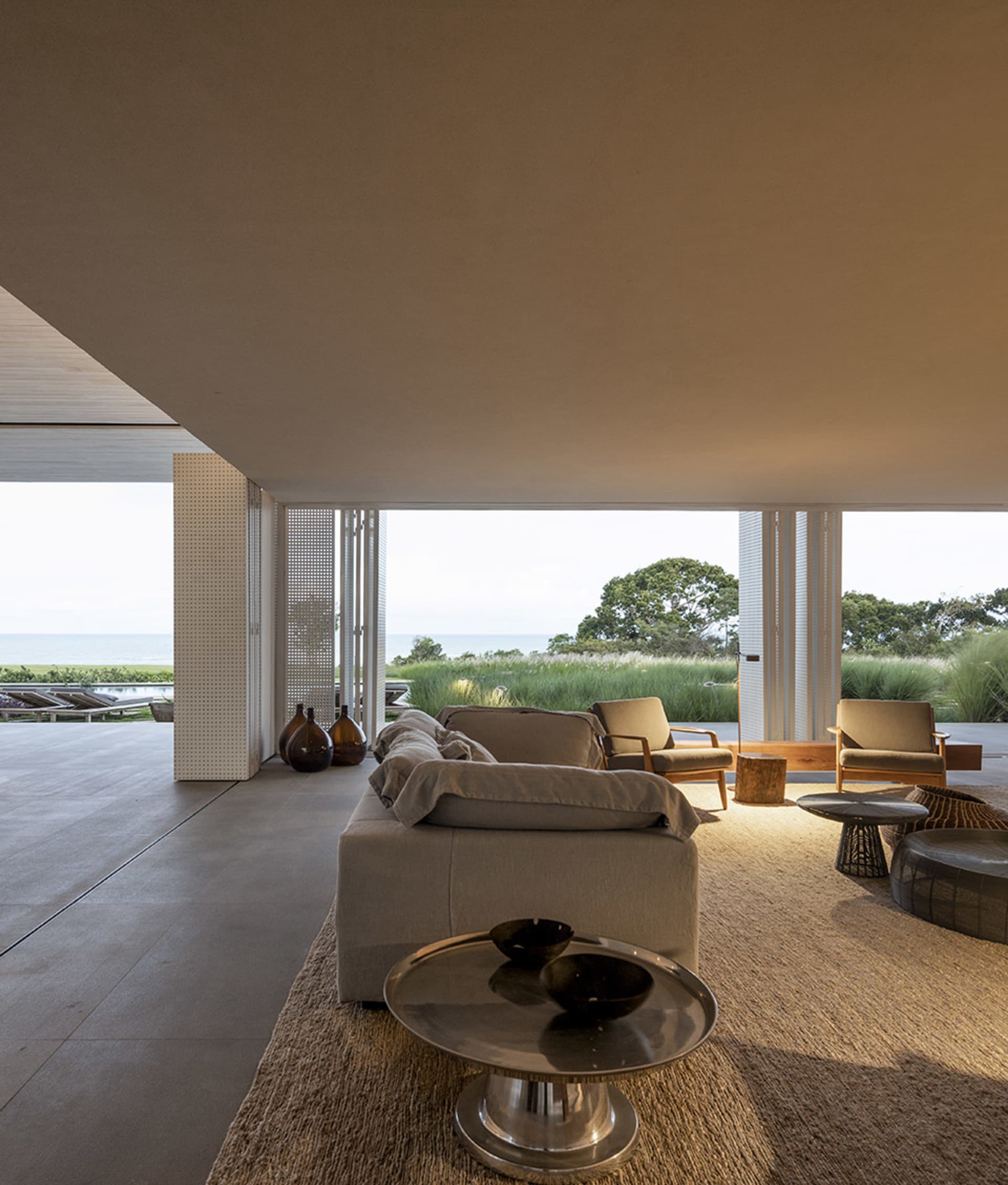 A modern living room with a concrete floor, featuring minimalistic furniture and a view of the ocean.