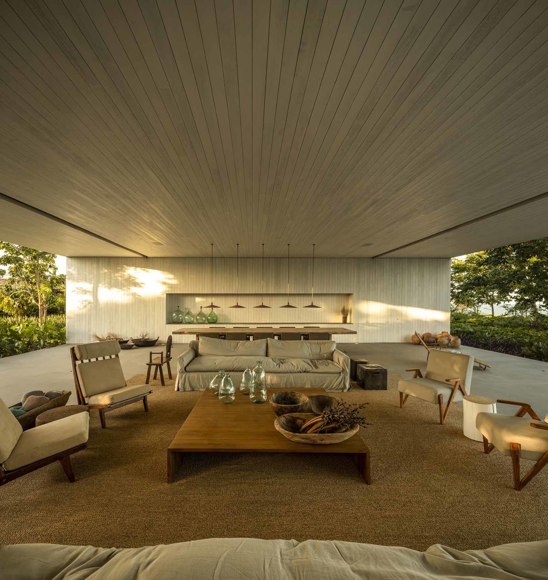 Modern living room with concrete walls and floor, featuring a low-slung sofa, wooden coffee table, and hanging pendant lights