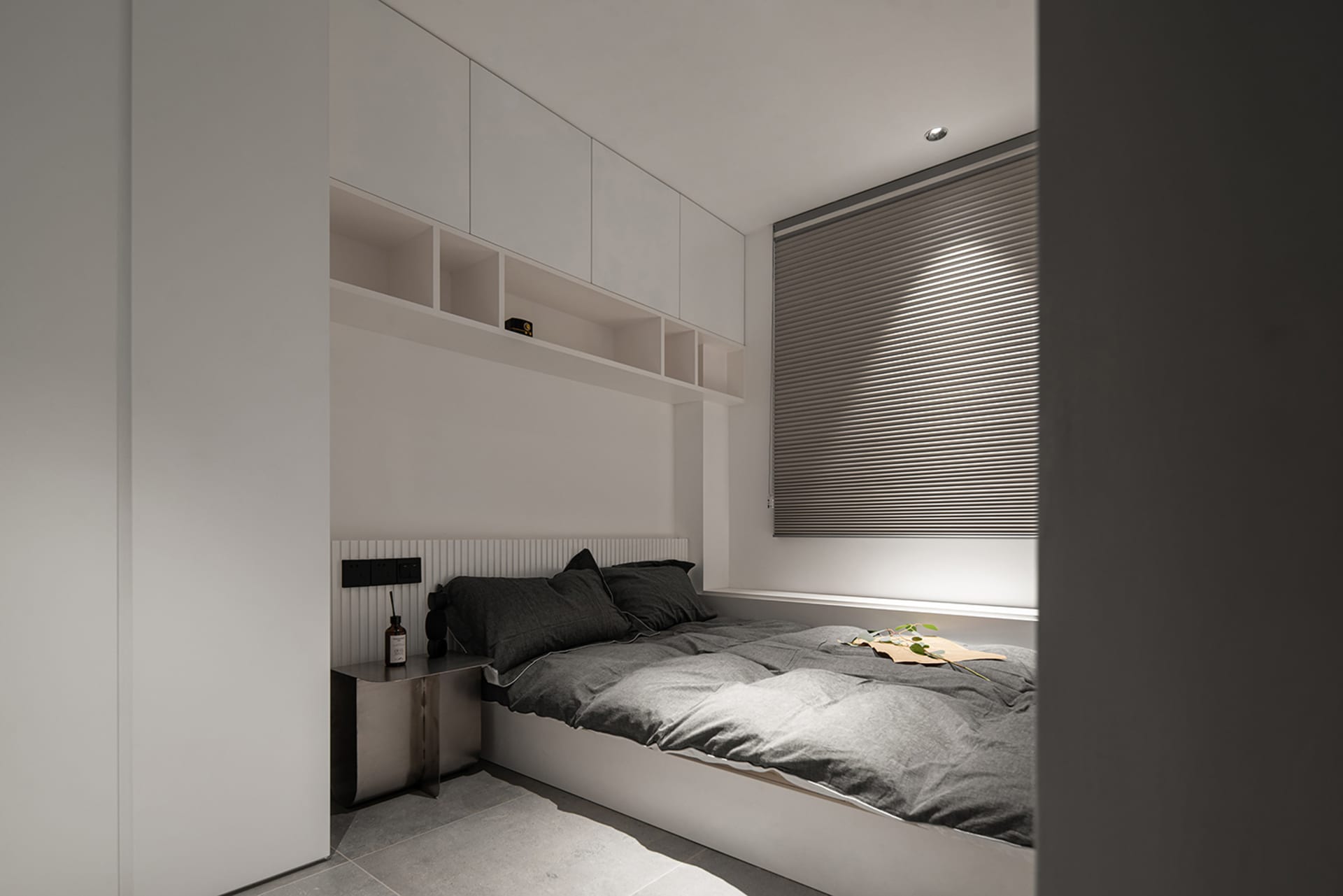 A minimalist bedroom featuring neutral-toned textiles on a built-in bed with integrated storage and a simple headboard