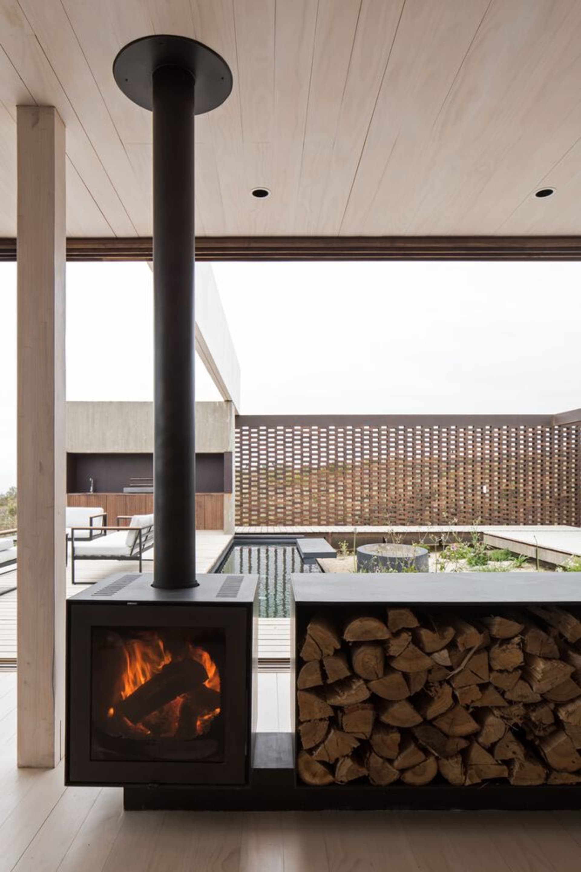 Modern industrial outdoor living space with a concrete fireplace, metal chimney, and wooden accents surrounded by a metal mes
